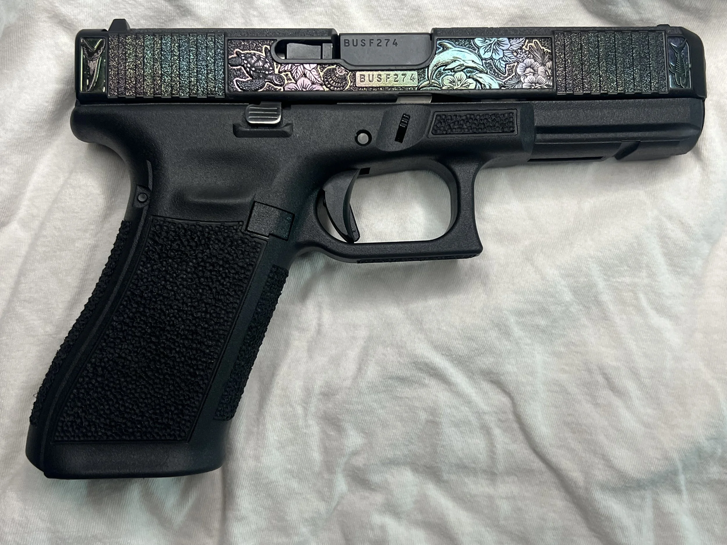 Custom Glock® 40 featuring decorative ocean scene slide engraving with colorful etched artwork and a black hand-stippled frame, showcasing detailed craftsmanship and personalized design work.