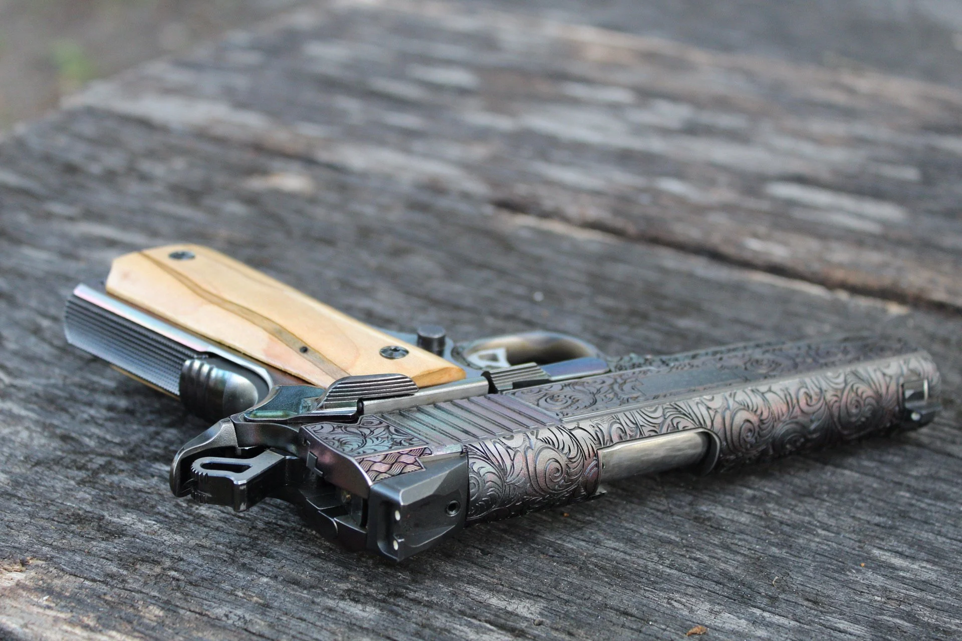 One-of-a-kind Ruger® 1911 featuring intricate scroll engraving, iridescent metal finish, and wood grip panels, custom designed and engraved for a client.