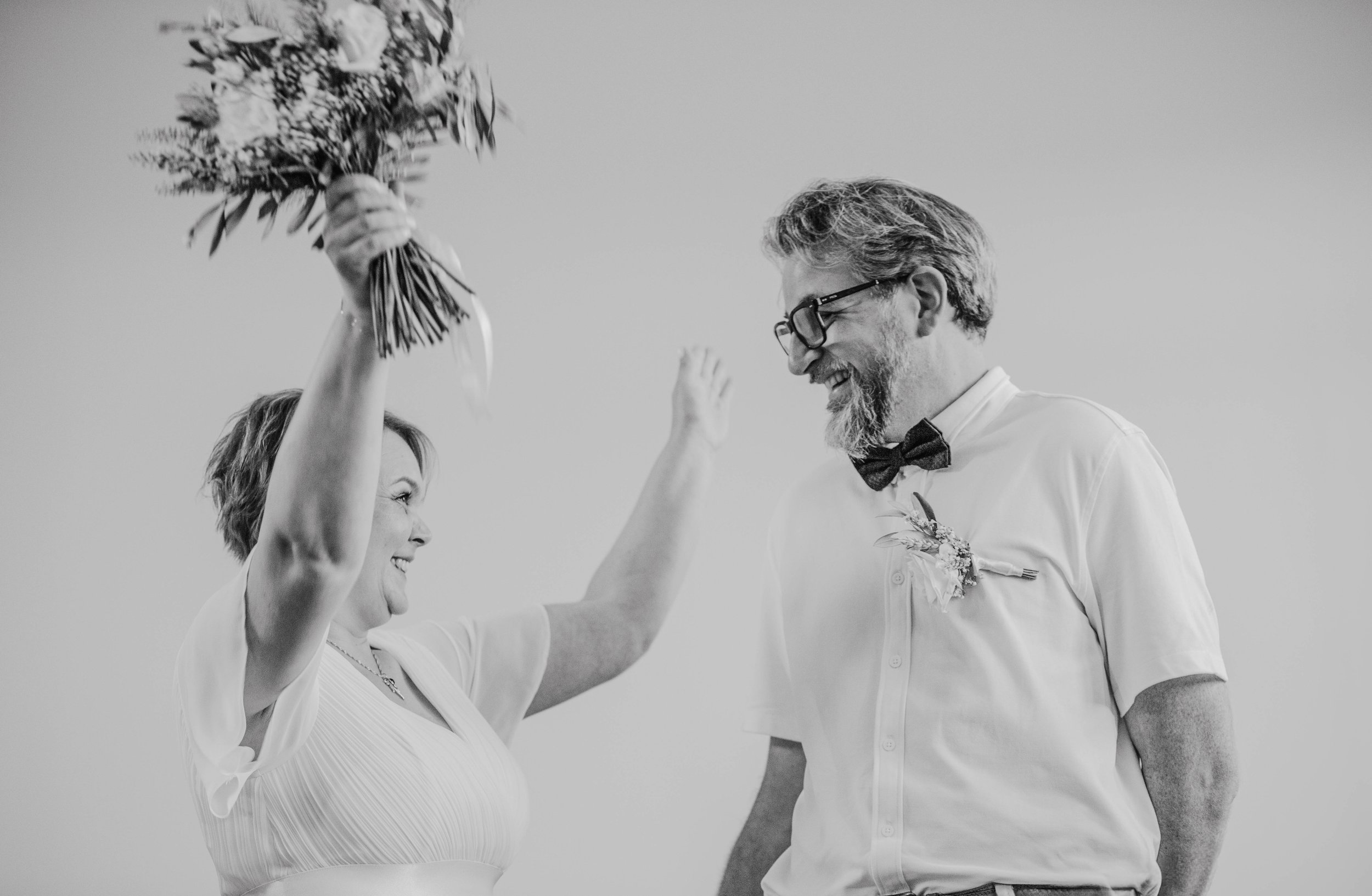 Une femme souriante donne un bouquet de fleurs à un homme souriant, tous deux habillés de manière habillée, lors d'une célébration ou d'un mariage.