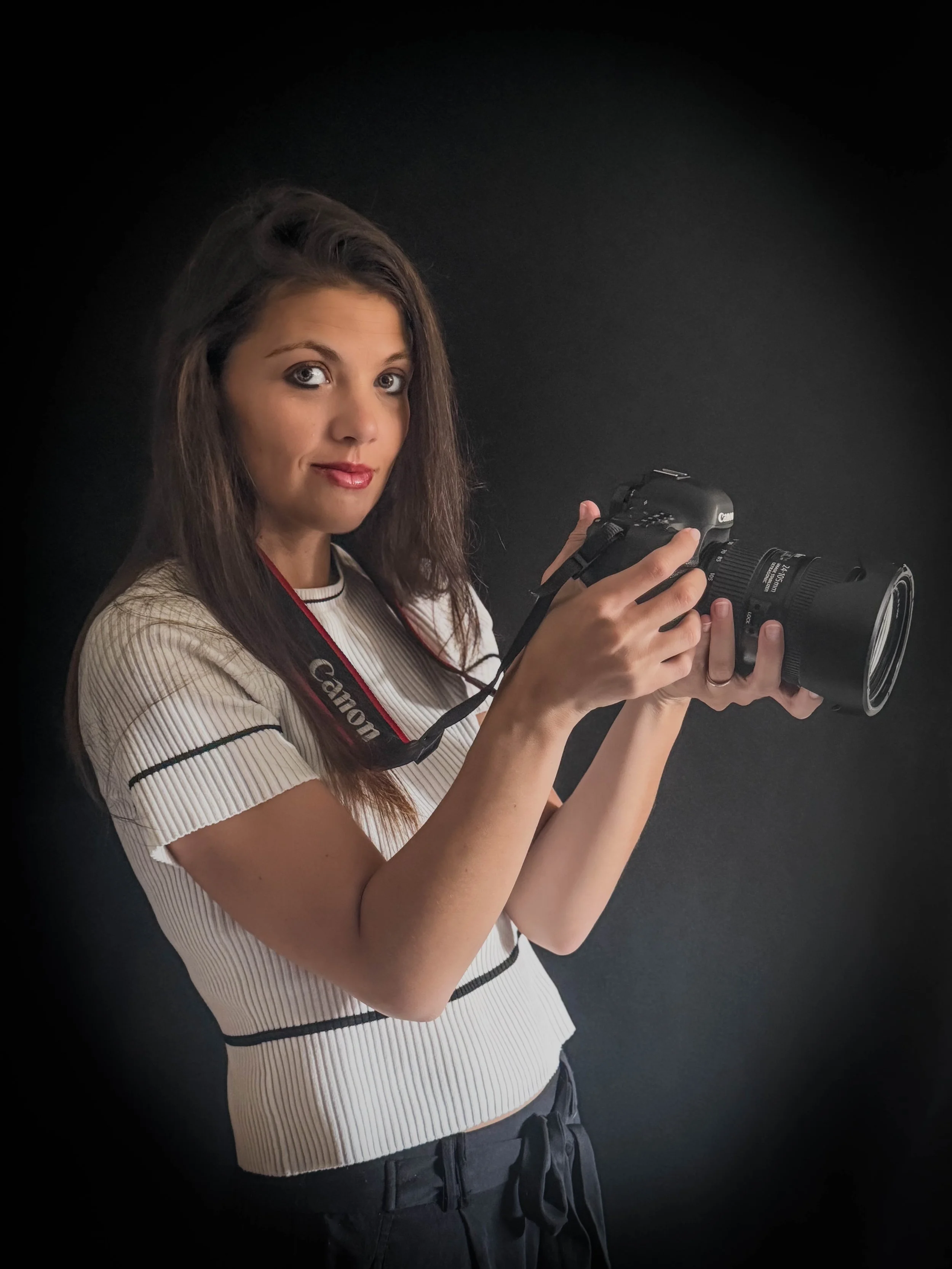 Jeune femme tenant un appareil photo Canon contre un fond noir.