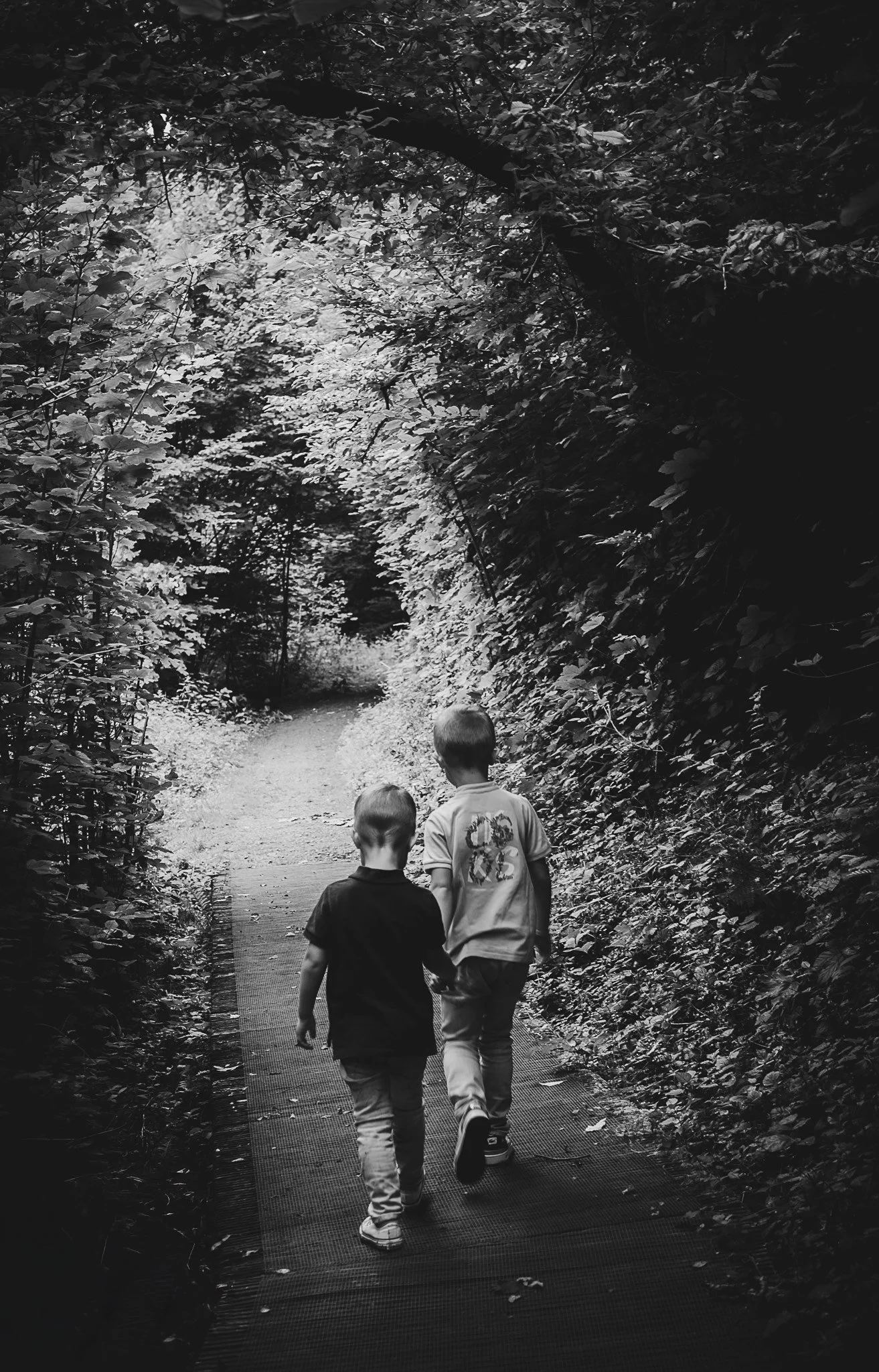 Deux enfants marchant côte à côte sur un sentier forestier en noir et blanc.