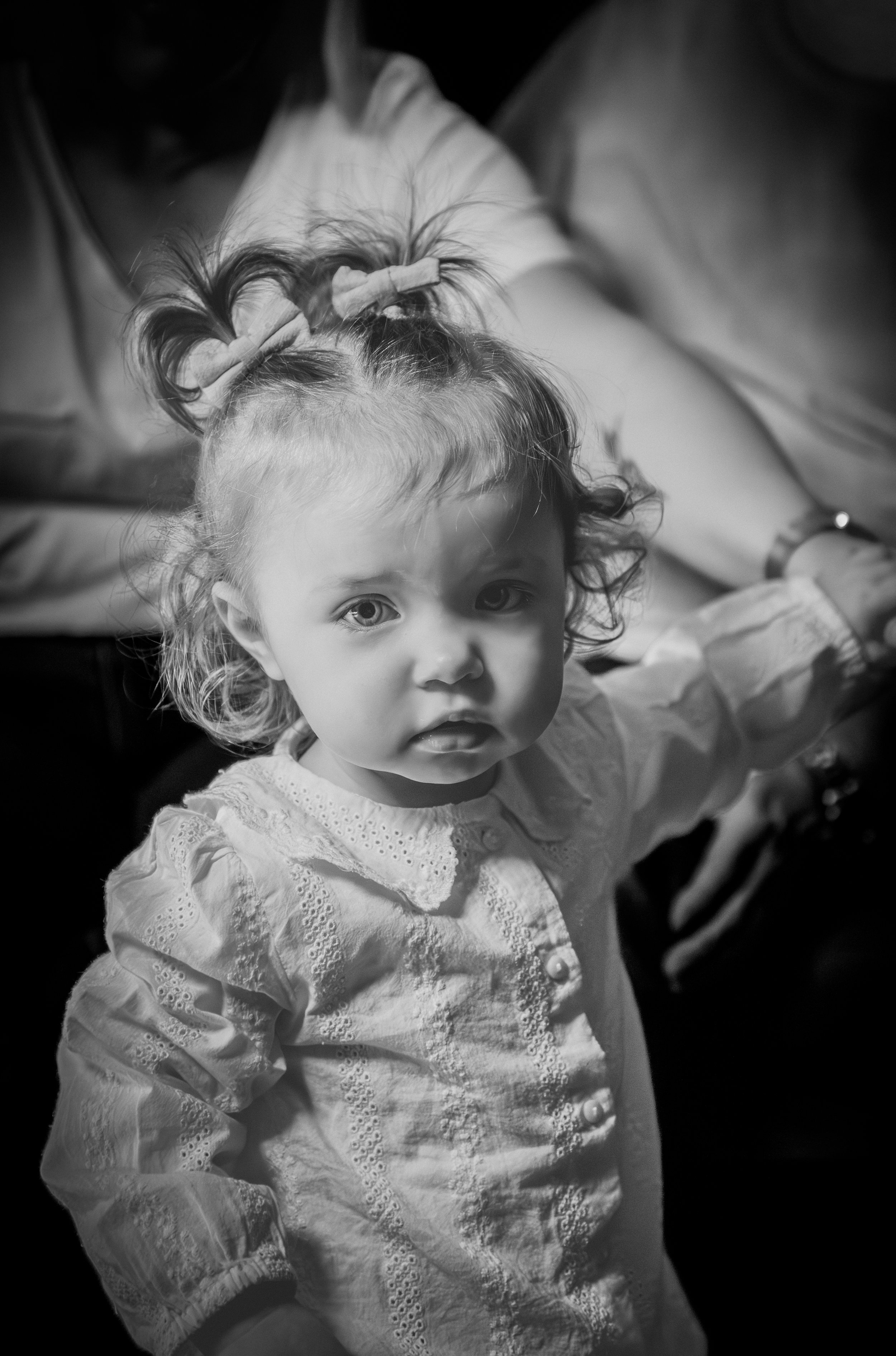 Jeune fille aux cheveux curly attachés avec des rubans, portant une chemise en dentelle, regardant vers l'objectif, en noir et blanc.