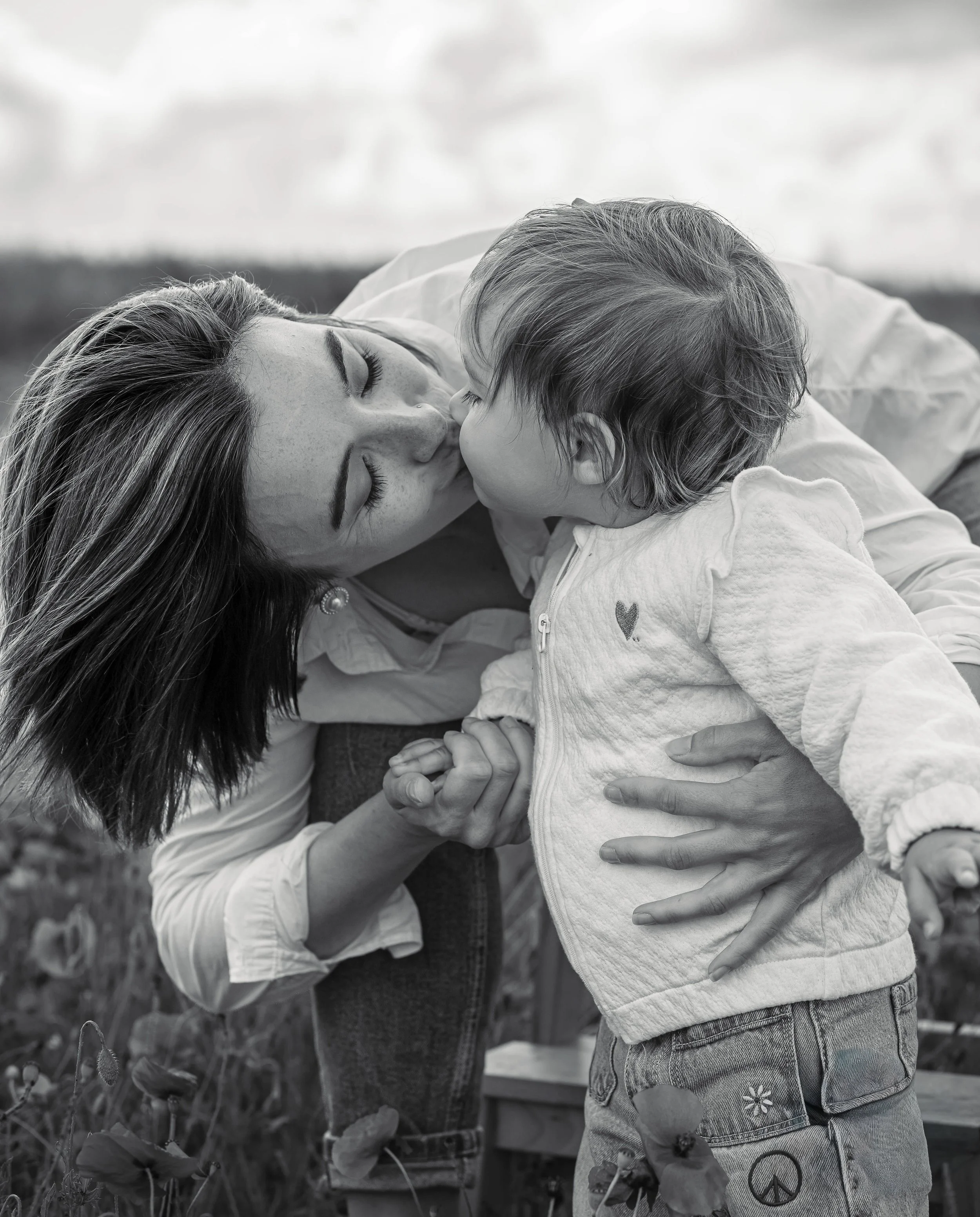 Une femme et un jeune enfant se donnent un bisou en plein air, en noir et blanc.