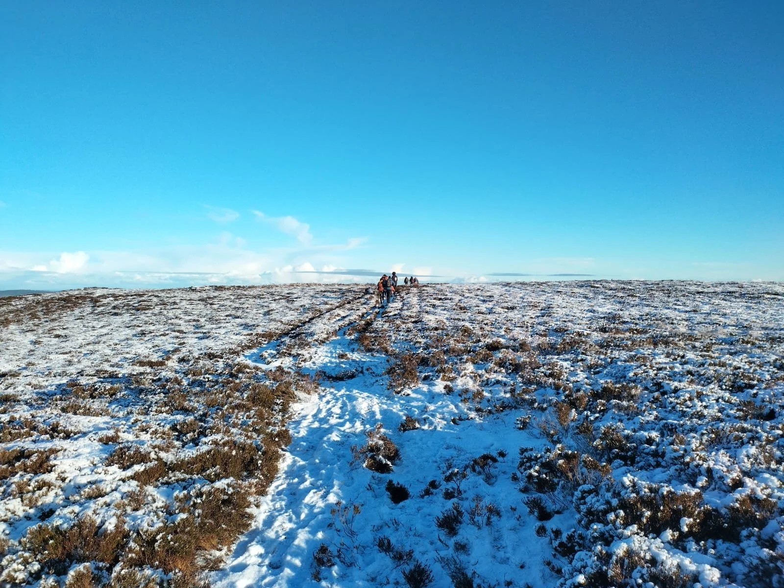 A group of people walking on a snow-covered field under a blue sky with some clouds.