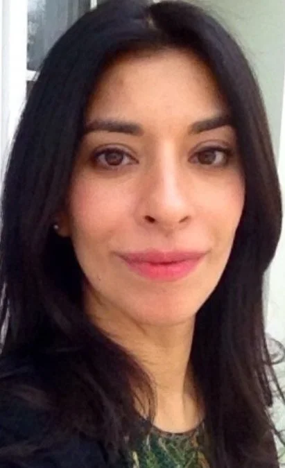 Close-up of a woman with dark hair and a slight smile, wearing makeup and a dark top.
