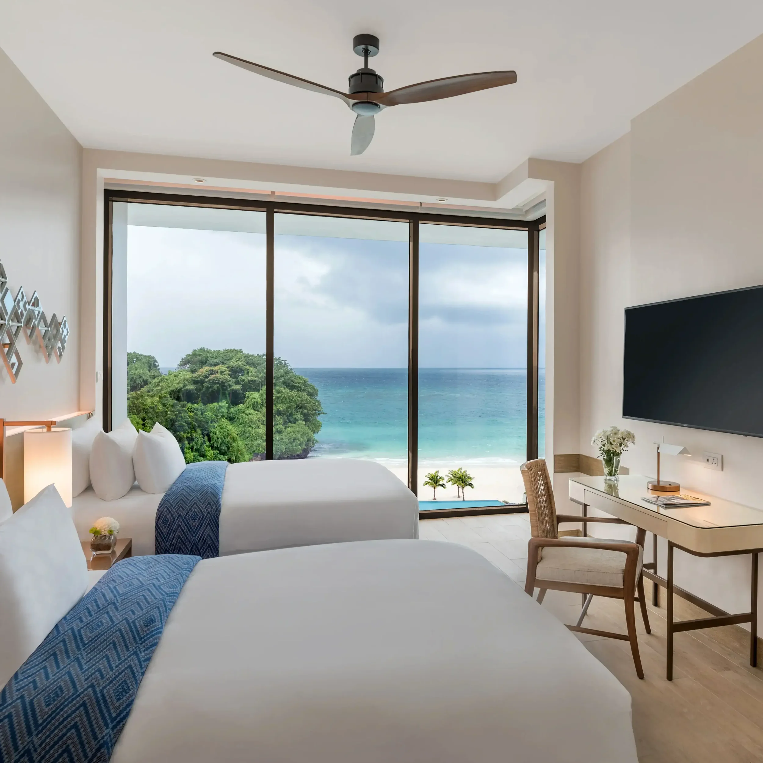 Crimson Boracay Suite Room with two beds, large window with ocean view, tropical trees, and beach, modern decor with desk, chair, and TV.