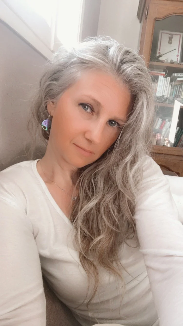 Une femme aux cheveux gris photographiée dans un intérieur lumineux.