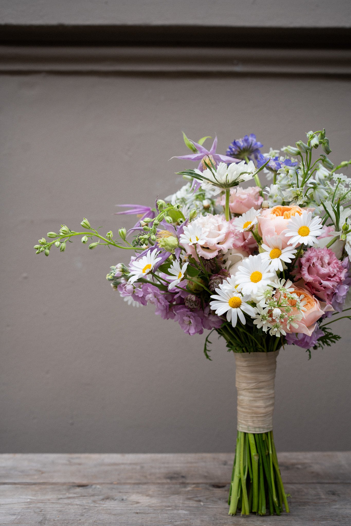 Bunter Blumenstrauß mit Weiß, Rosa, Lila und Gelb, auf Holzuntergrund, gegen grauen Hintergrund
