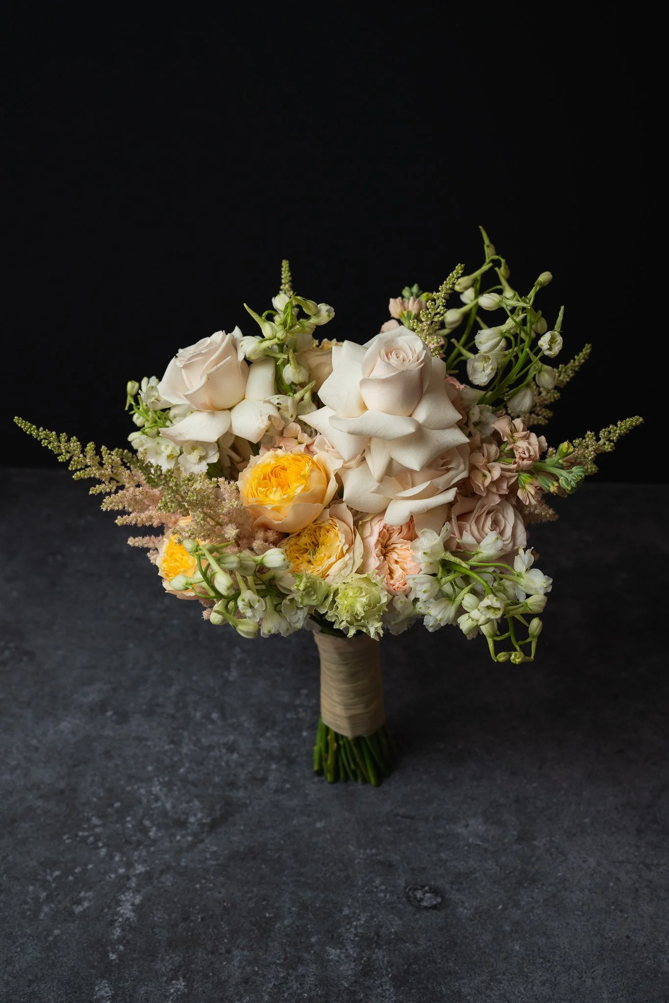 Hochzeitsstrauß mit weißen und gelben Blumen vor schwarzem Hintergrund.