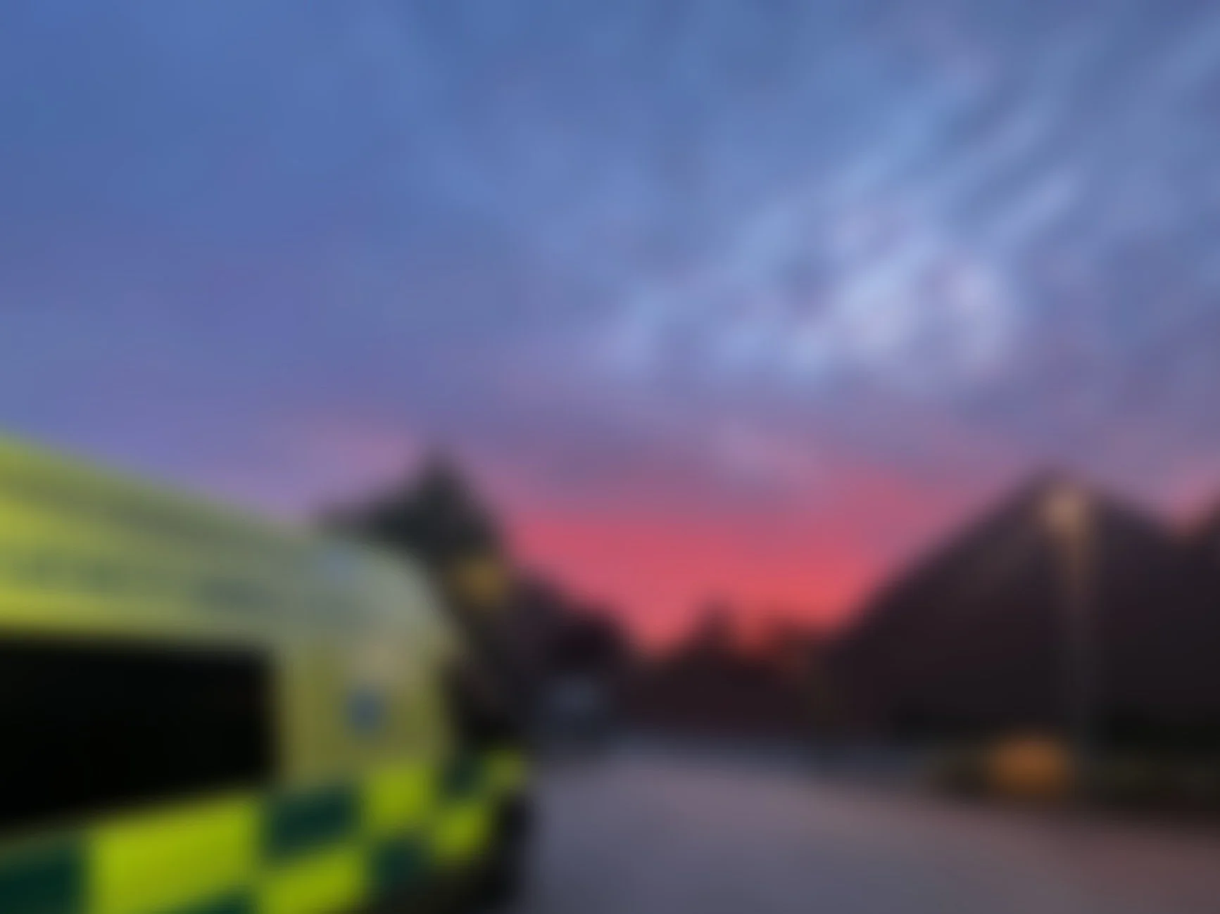 Blurred photo of an ambulance, with a vibrant sunset sky in the background.