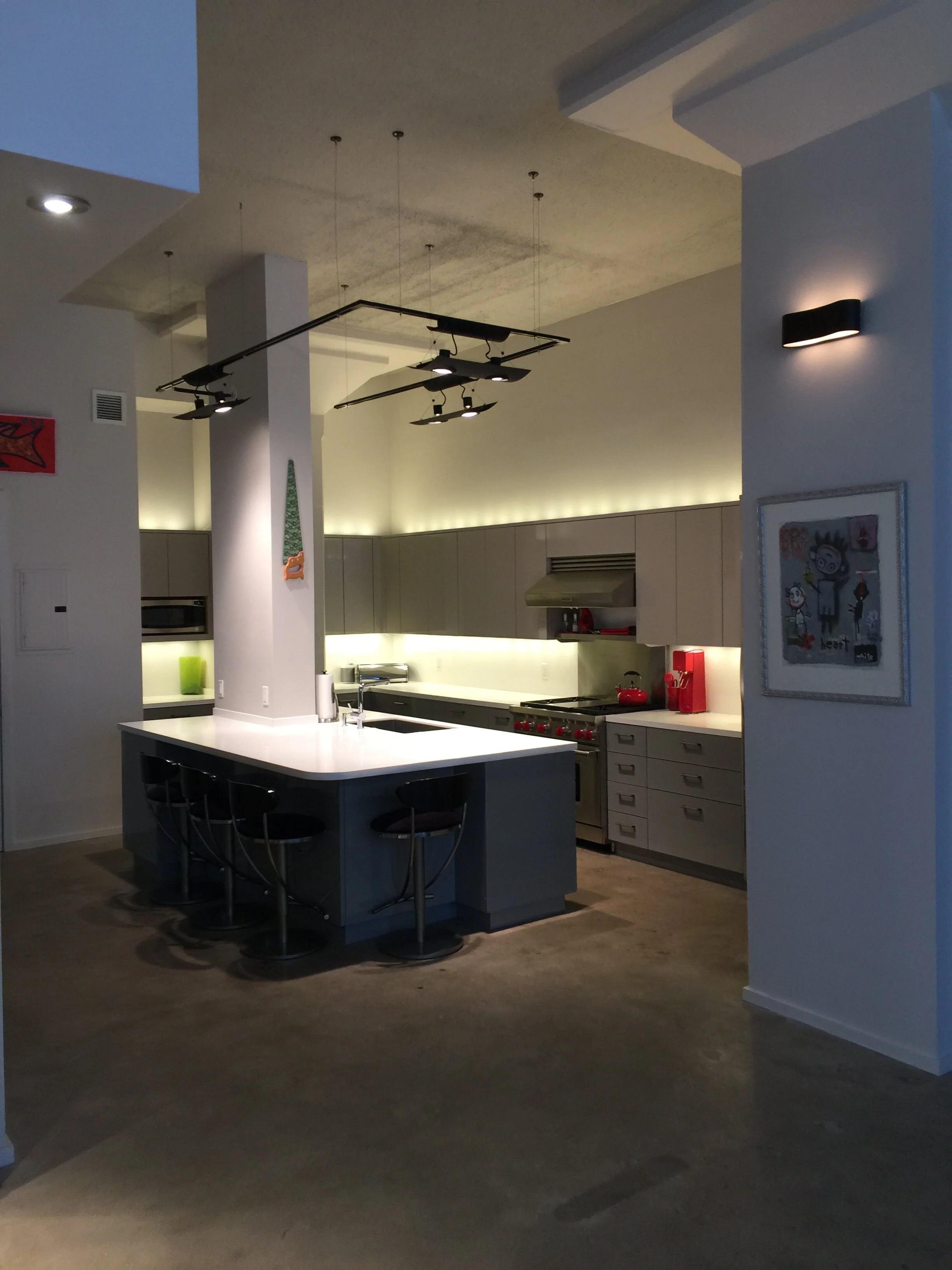Modern kitchen with white cabinets, stainless steel appliances, and a large white island with black bar stools. Dim lighting creates a cozy ambiance.