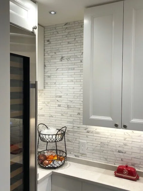 Kitchen corner with white marble backsplash, white cabinets, a black wire basket with oranges and apples, and a red toy phone on the countertop.