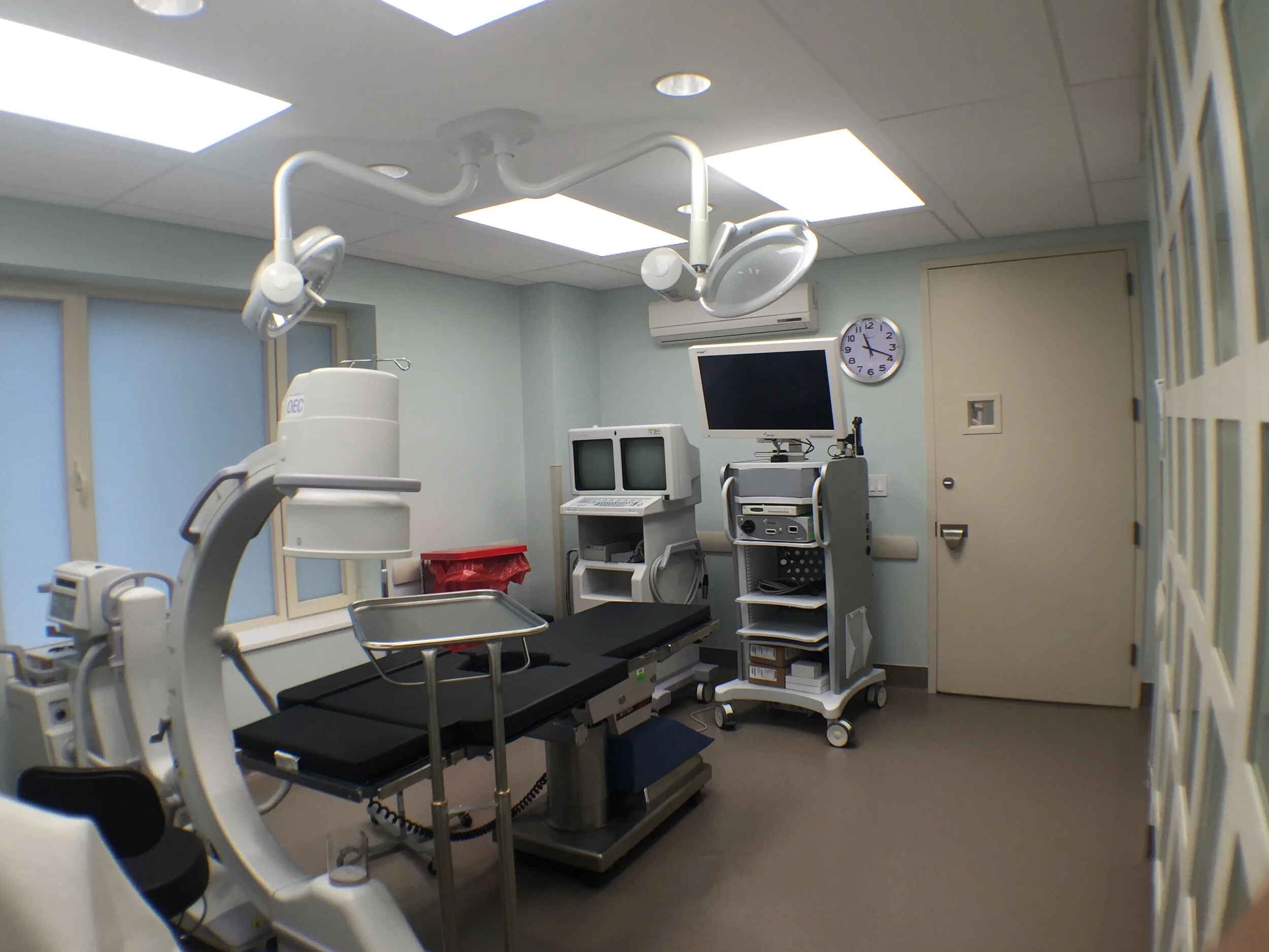 An empty hospital operating room with medical equipment, surgical lights, and monitors.