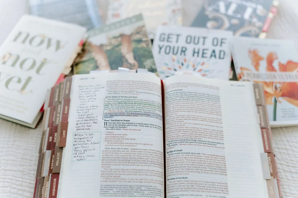 Open Bible with handwritten notes nearby, surrounded by various motivational and inspirational book covers.