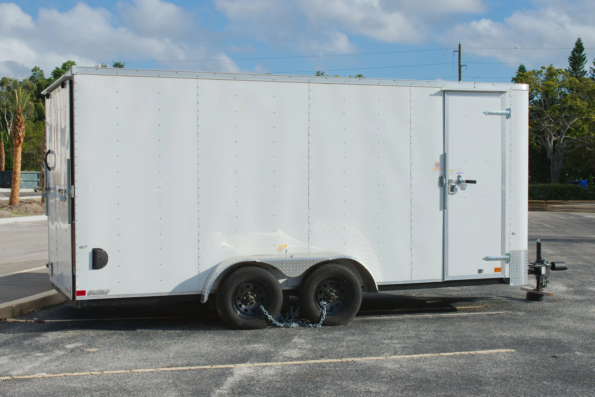 White enclosed truck trailer parked in an empty parking lot under a partly cloudy sky.