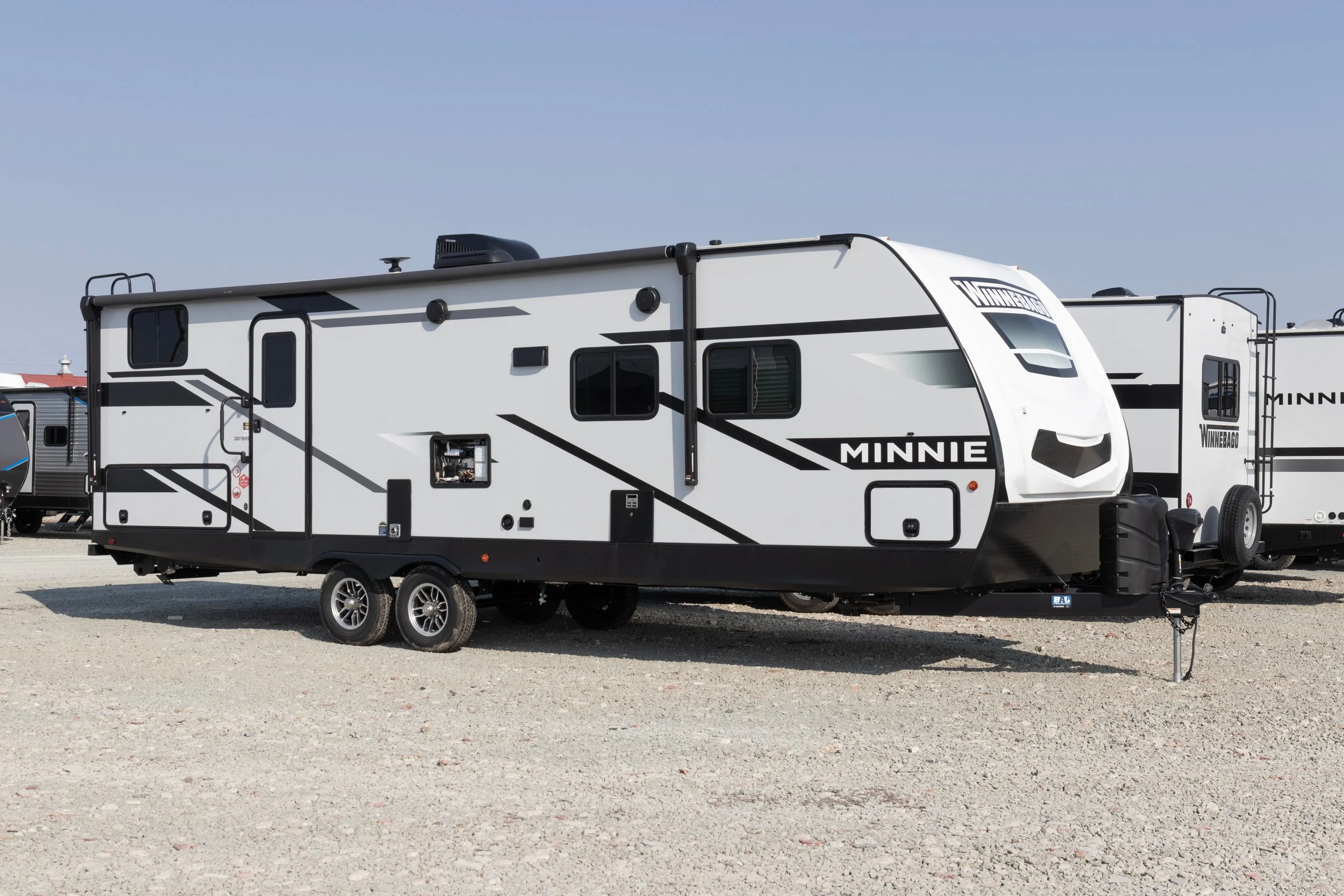 A white and black Winnebago Minnie travel trailer parked on a gravel lot.