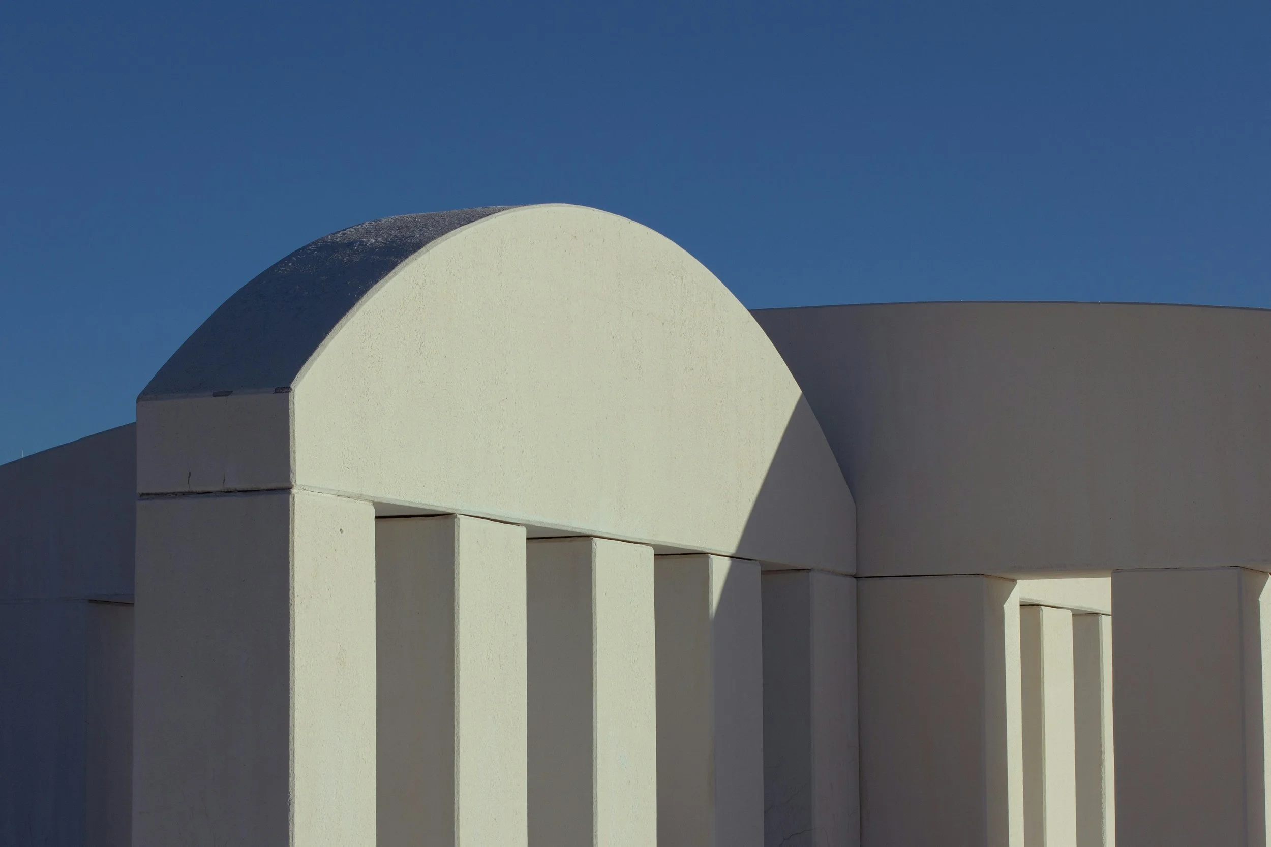 Close-up of a modern white architectural building with columns and curved roof against a clear blue sky.