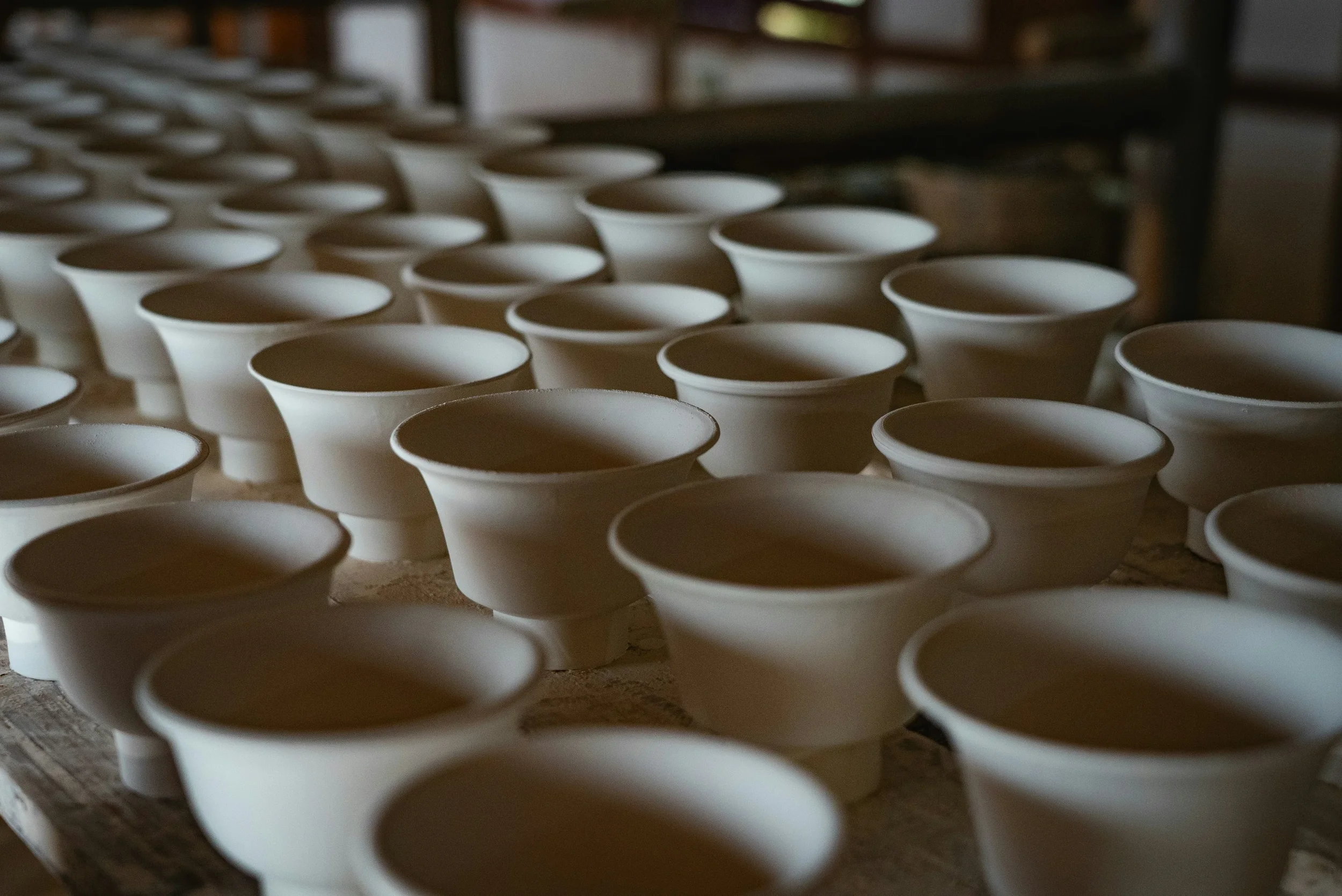 Rows of unfired ceramic cups arranged on a pottery workshop table