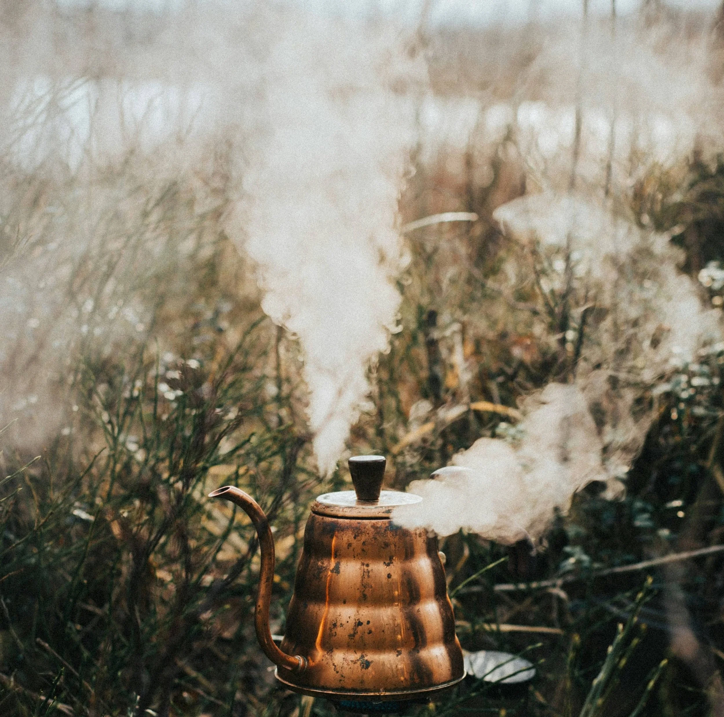 copper tea kettle boiling on an outdoors stove with steam billowing from the top