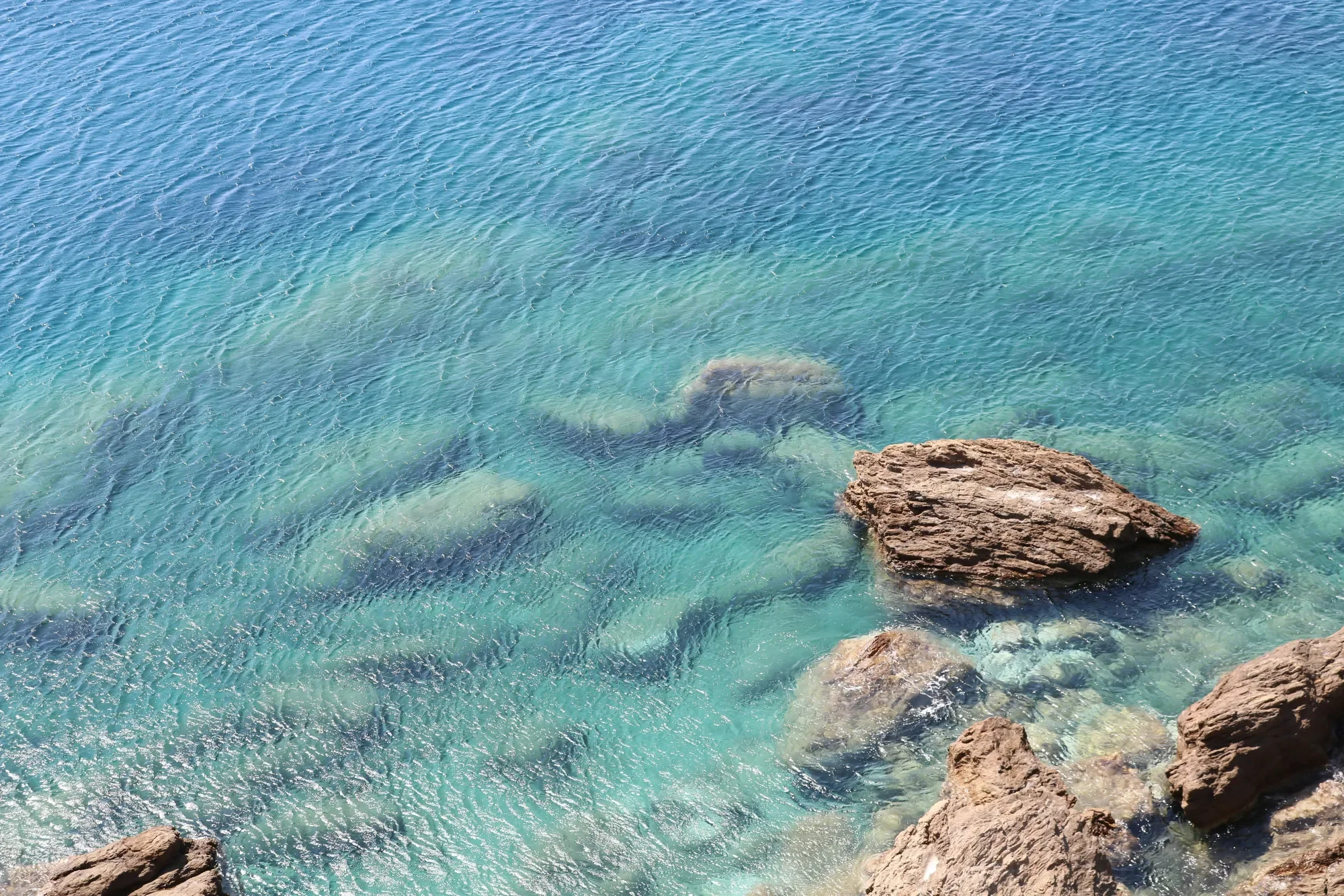 Clear turquoise water with dark rocks visible beneath the calm surface