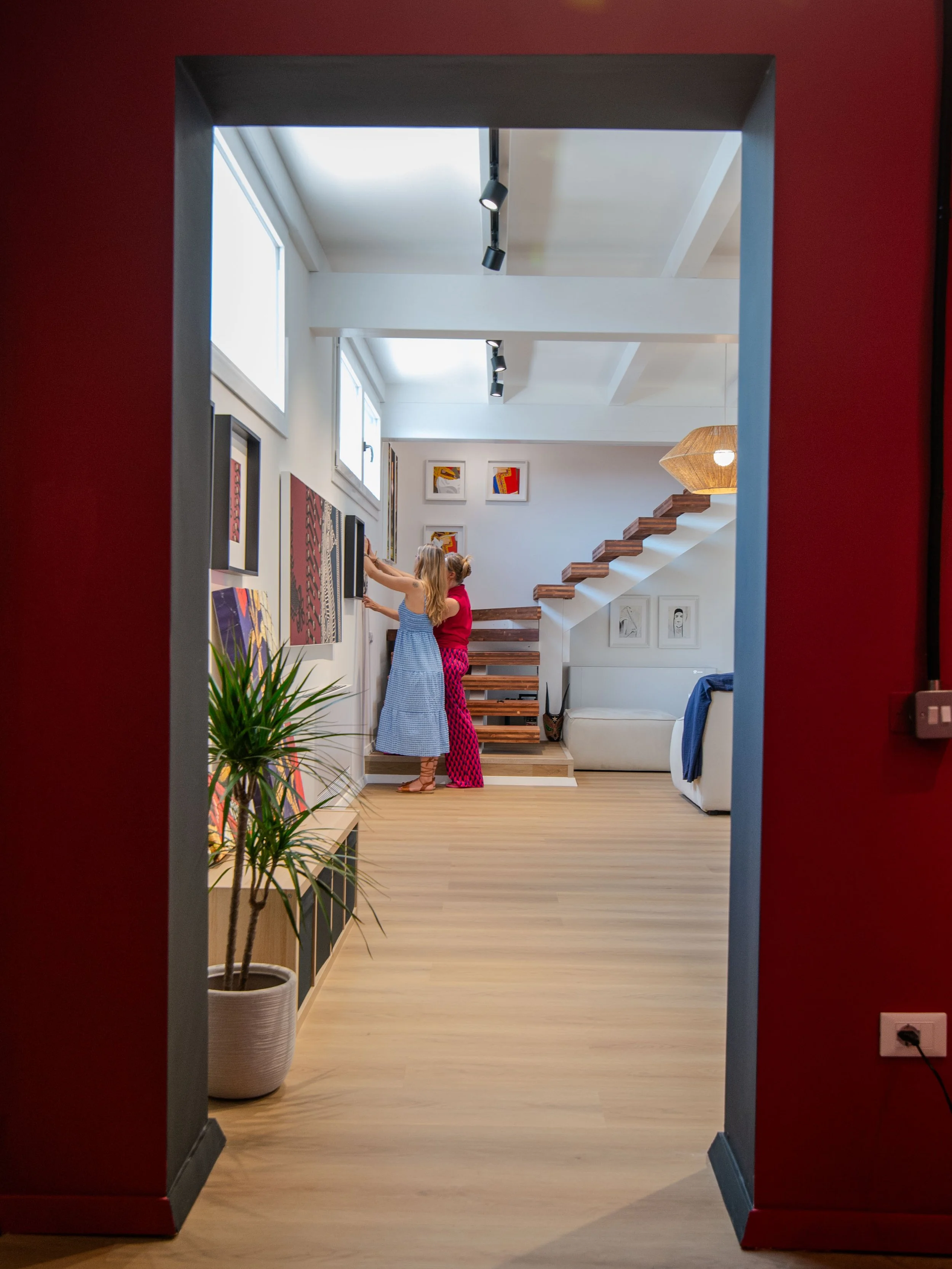 Due bambine sono appese a un quadro nella parete di un soggiorno moderno. La scena è vista da una porta aperta con pareti rosse.