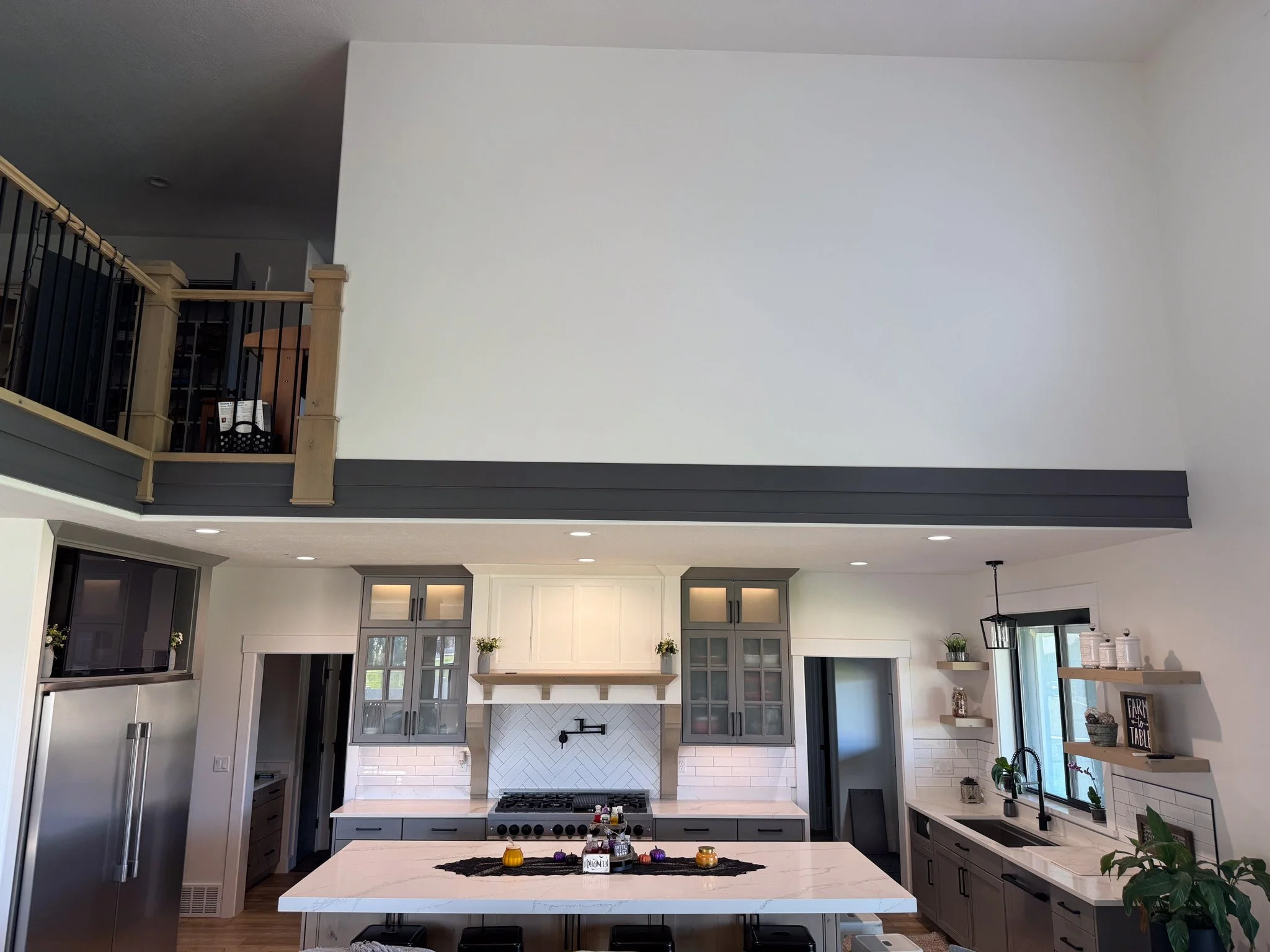 Modern kitchen with white and gray cabinetry, marble island, stainless steel appliances, and open shelving, with a balcony above.