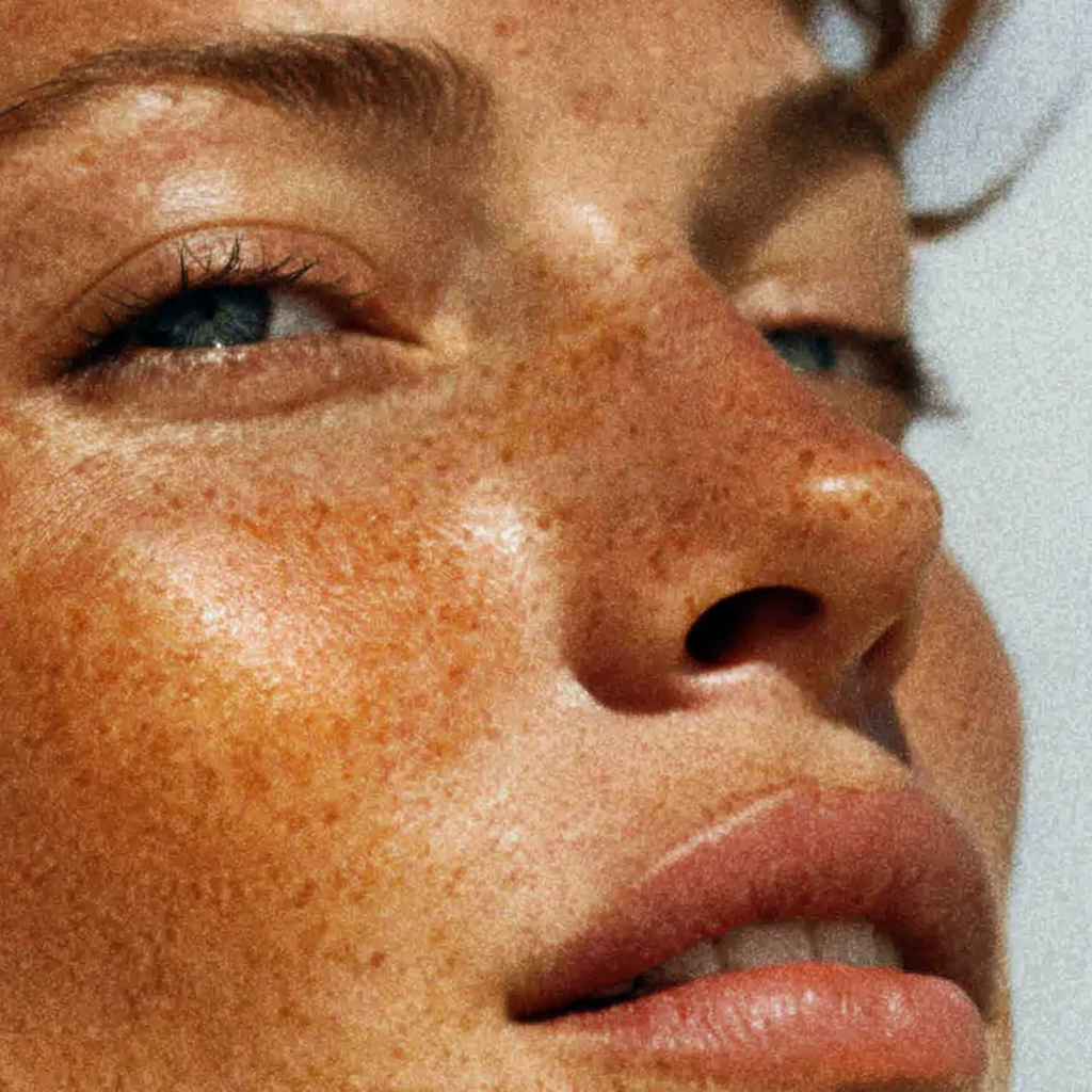 Close-up of a person's lips slightly parted, showing white teeth, with dewy skin and some light reflections.