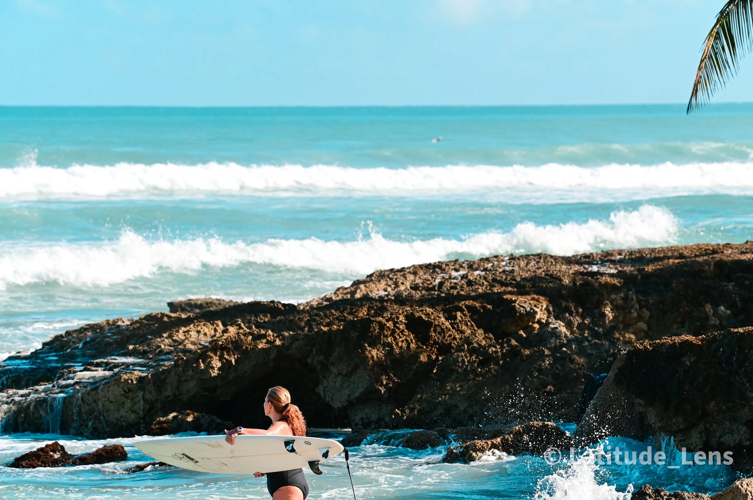 Surfer standing in the ocean with a board at sunset along a rocky puerto rico coastline