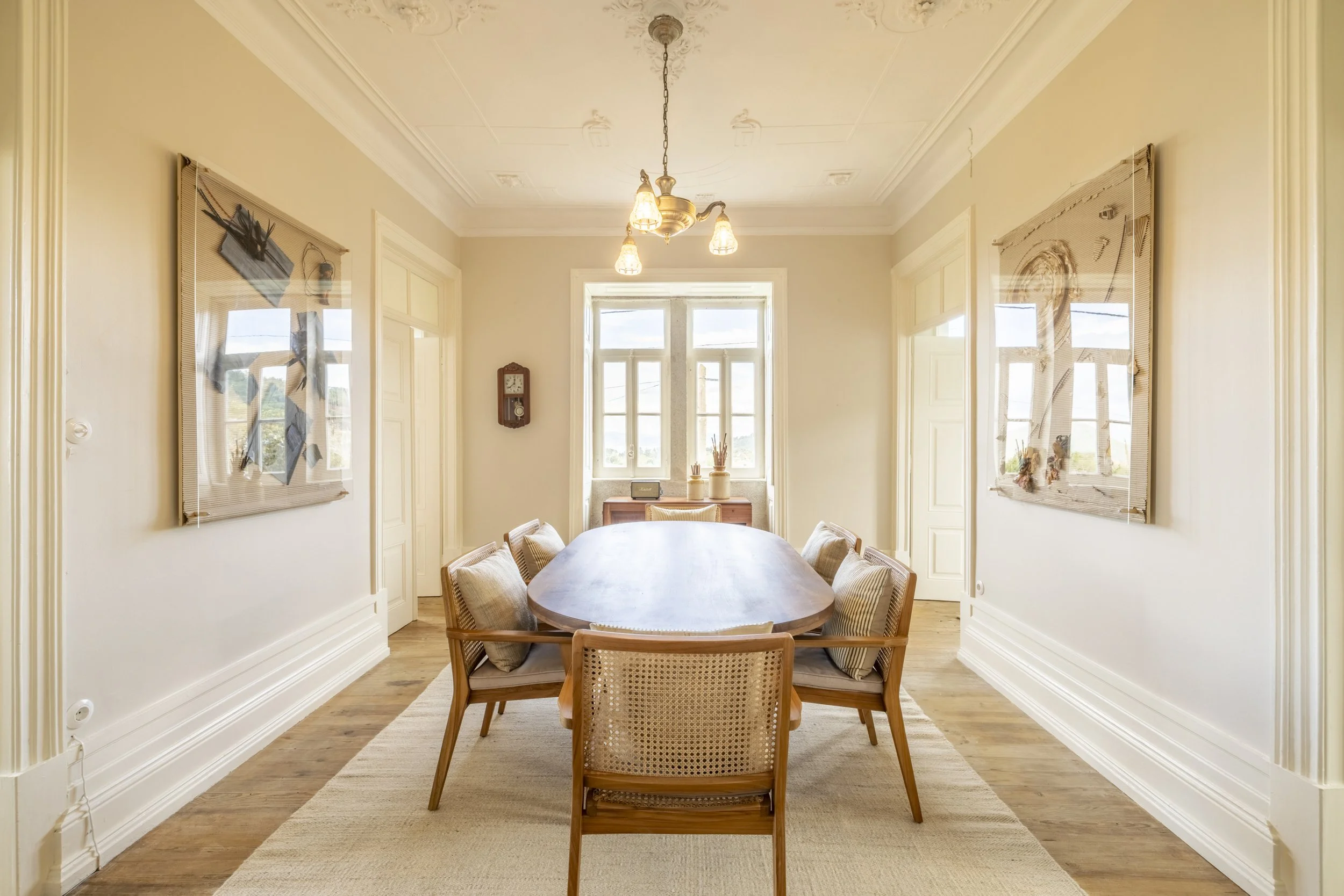 Sala de estar com janela em frente, mesa de jantar no centro e quadros nas paredes laterais