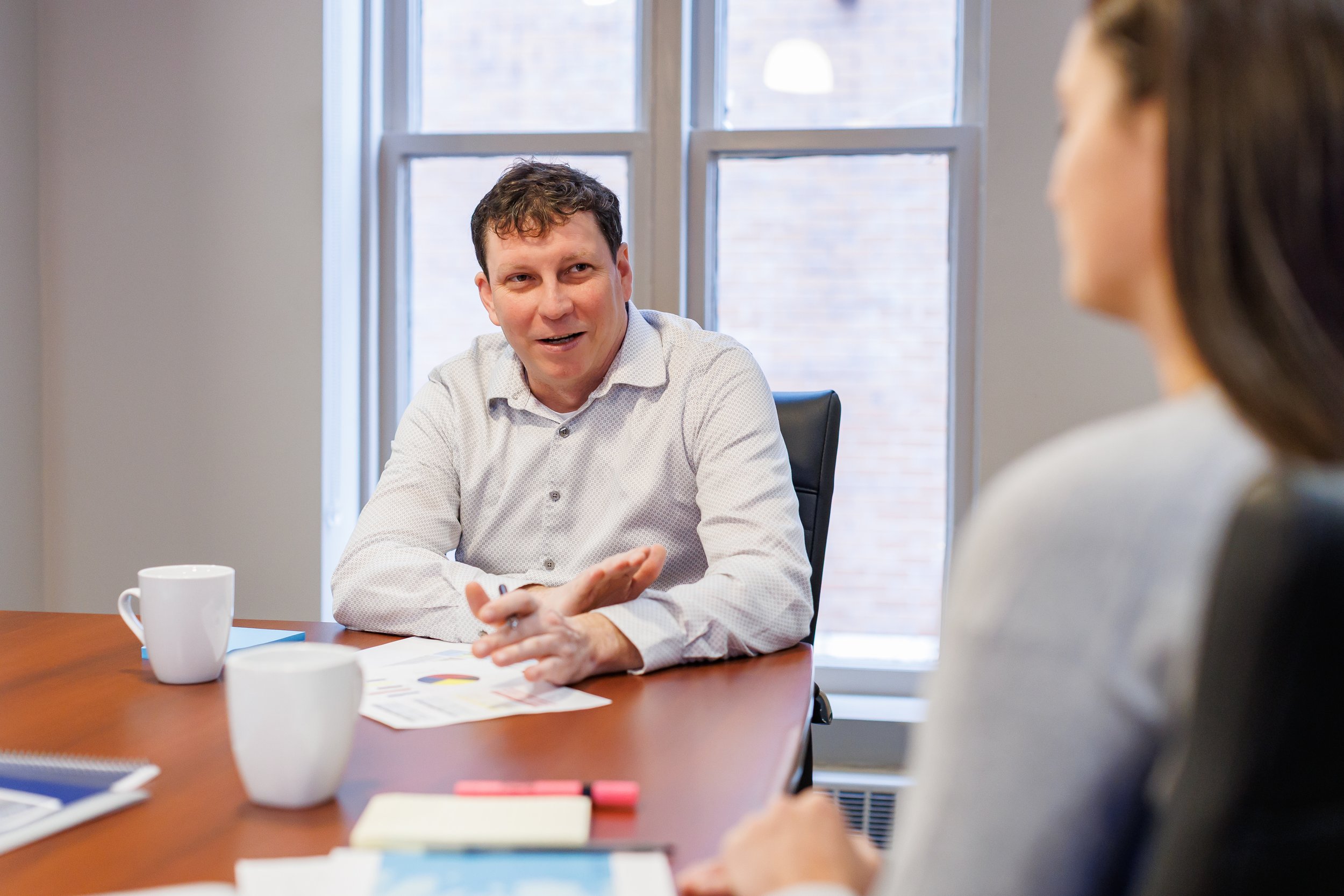 A man and woman having a business meeting in a bright office with large windows.