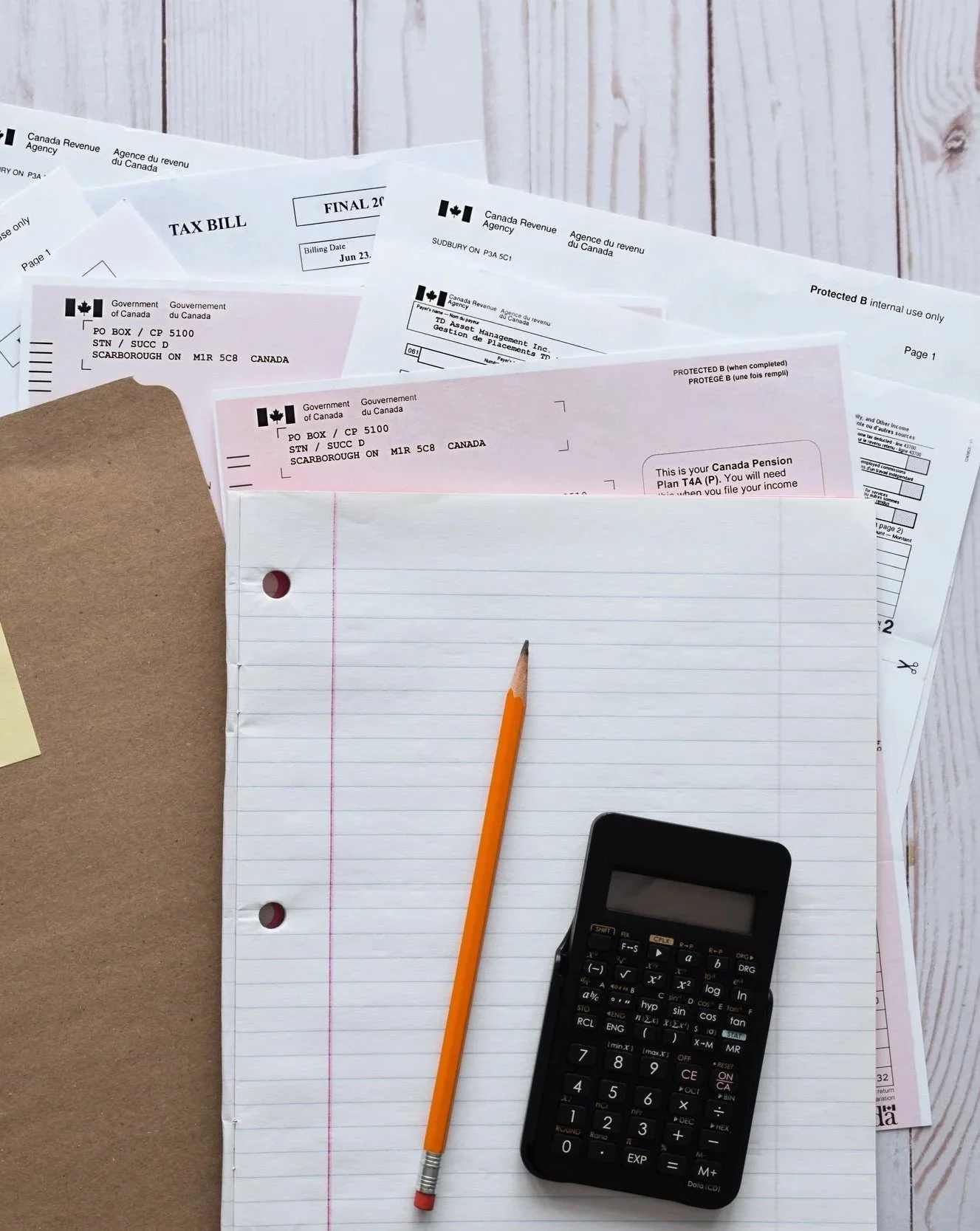 Several tax documents, a lined notebook paper, a yellow pencil, and a calculator on a white wooden surface.