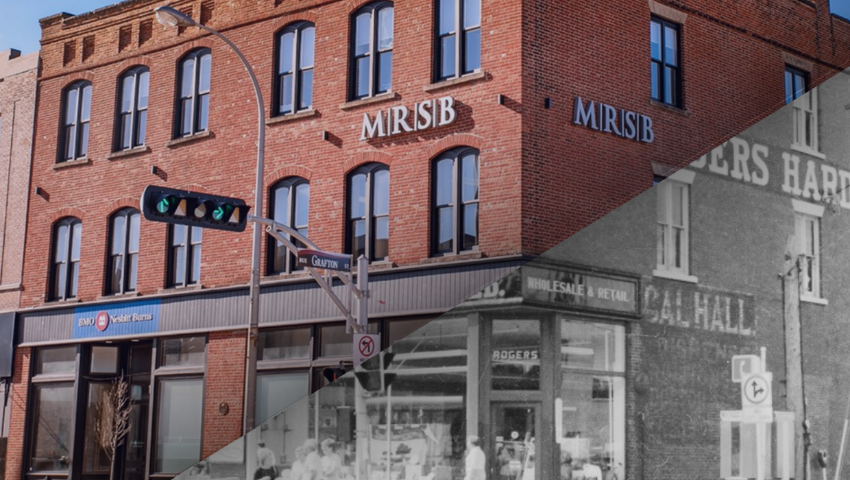 A corner building with a brick facade, featuring multiple windows and store signs for MIRSIB and BMO Nesbitt Burns. A street sign marked Grafton Street is visible, along with traffic lights and a streetlamp.
