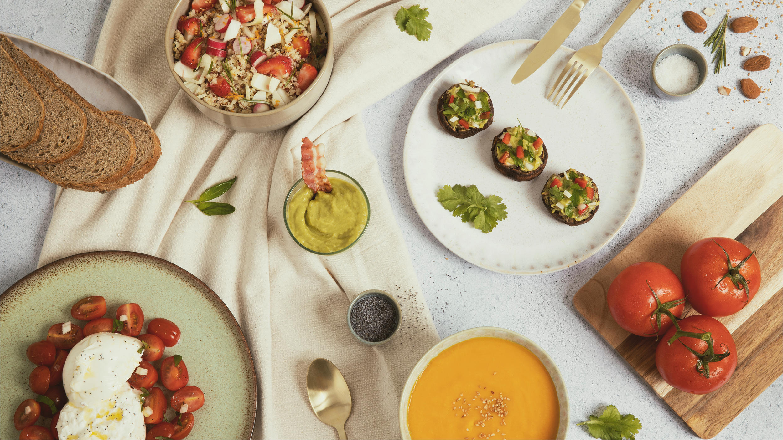 Table de petit déjeuner avec tomates, œufs, guacamole, pain complet, salade de tomate et quinoa, champignons farcis, soupe à la courge, et diverses garnitures.
