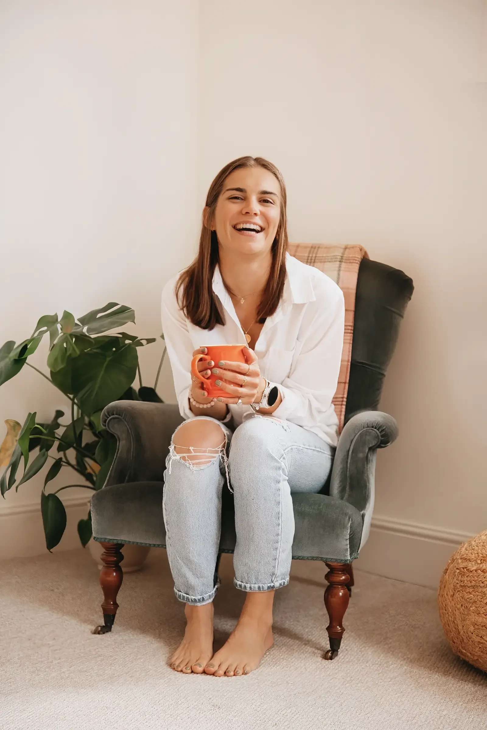 Portrait of Georgina Howell sitting and laughing whilst holding an orange mug.