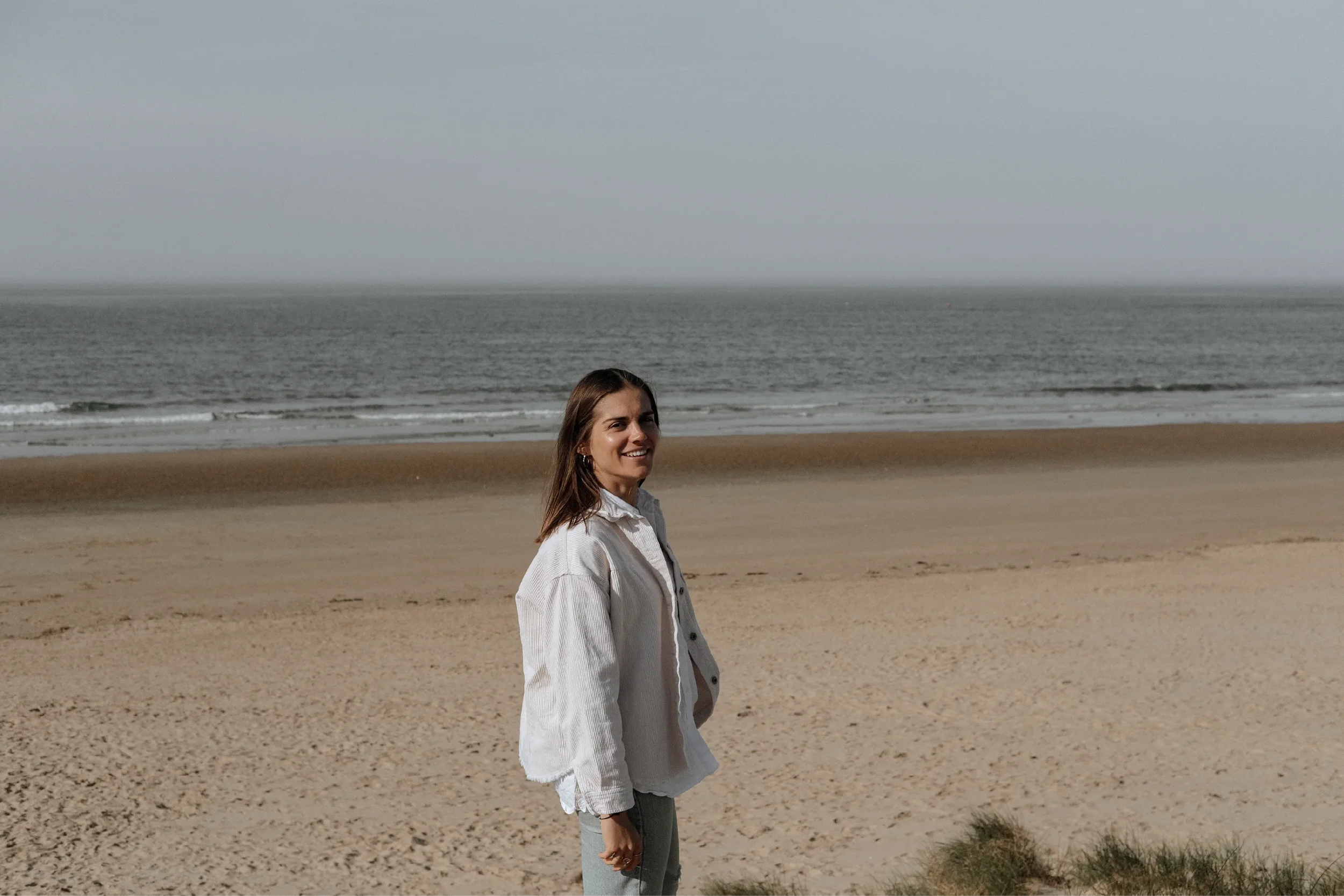 Portrait of Georgina Howell standing on the beach with the sea behind her.