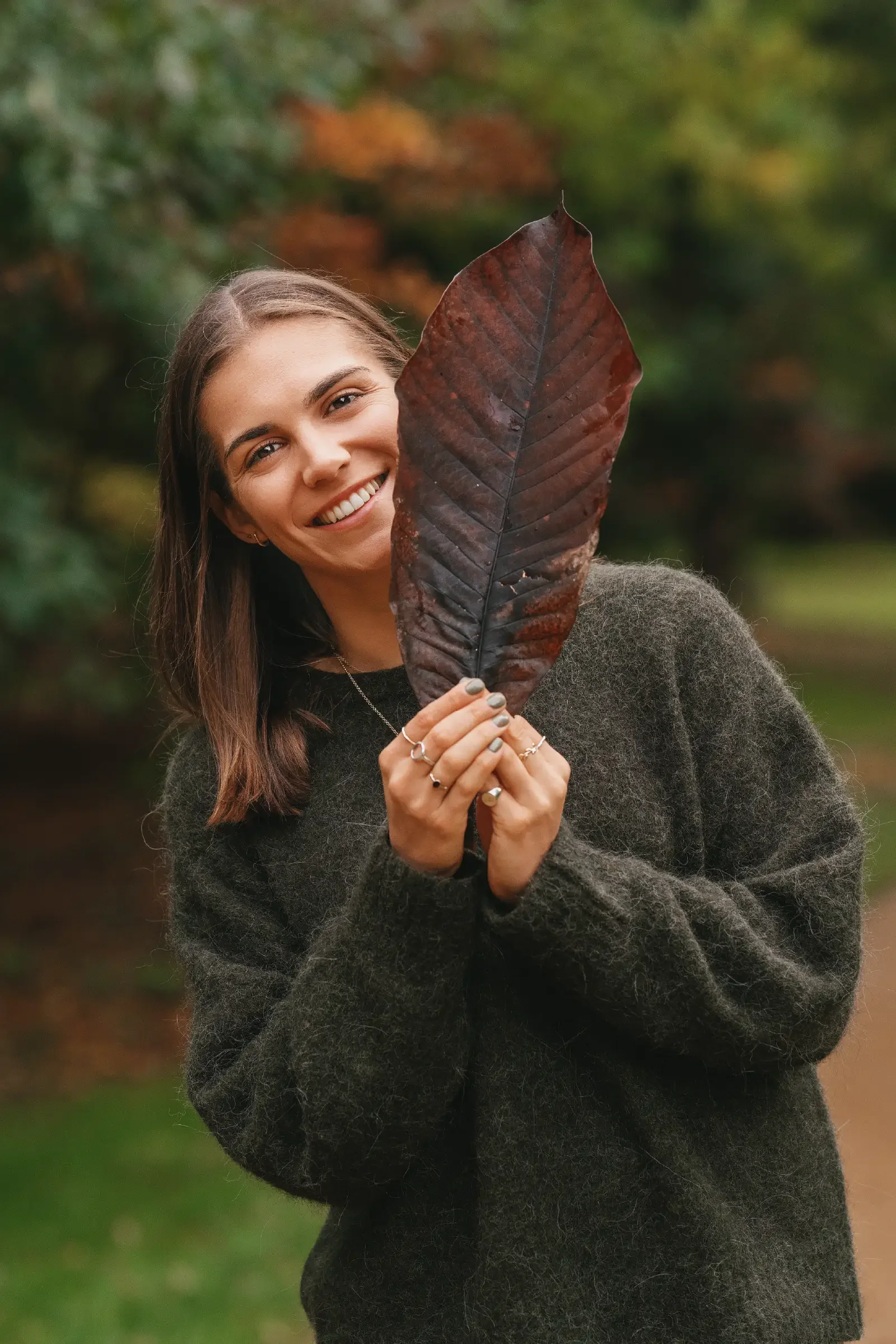 Portrait of Georgina Howell poking her head out from behind the big brown leaf.