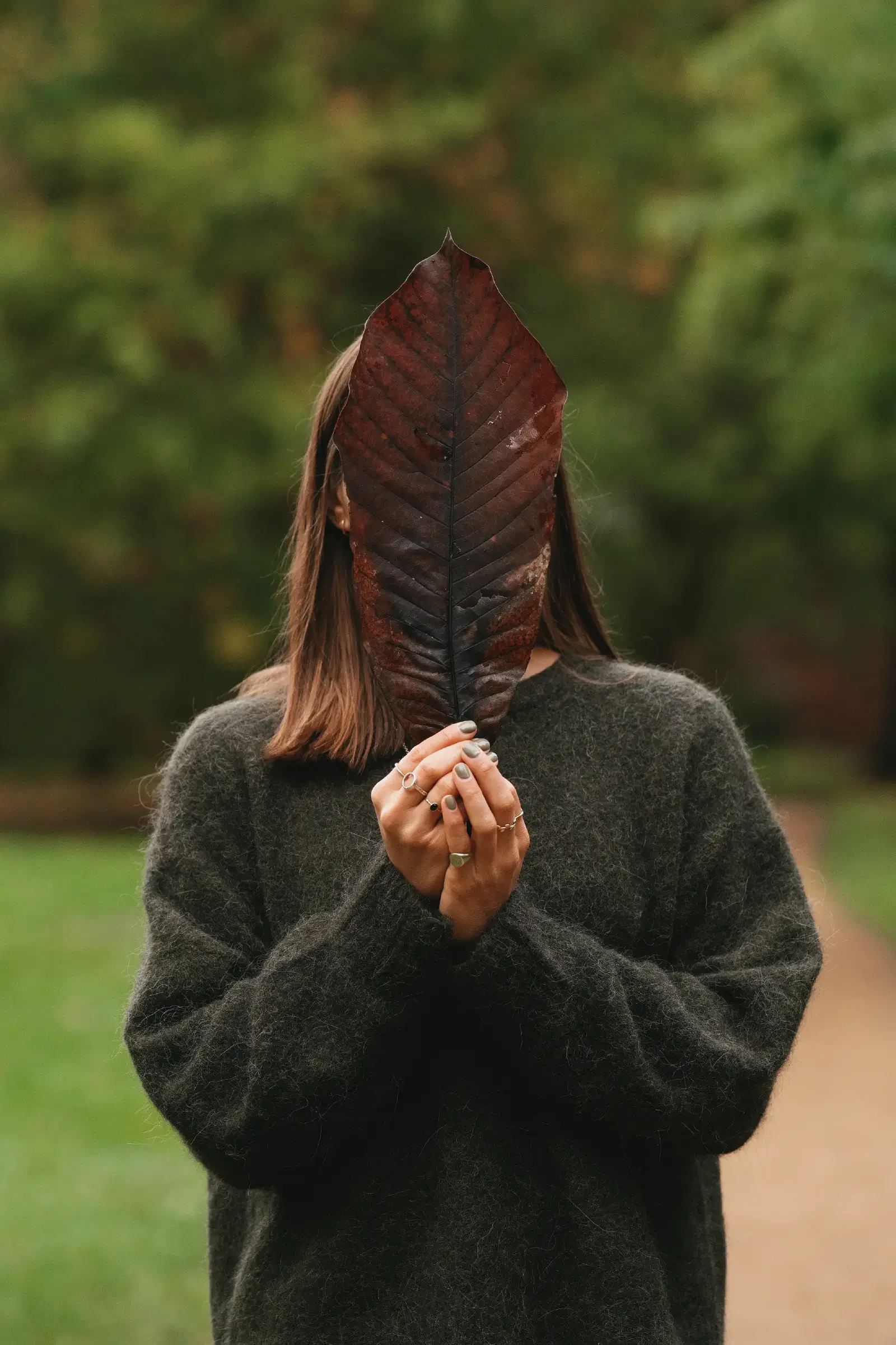 Portrait of Georgina Howell, hiding her face behind a big, brown leaf.