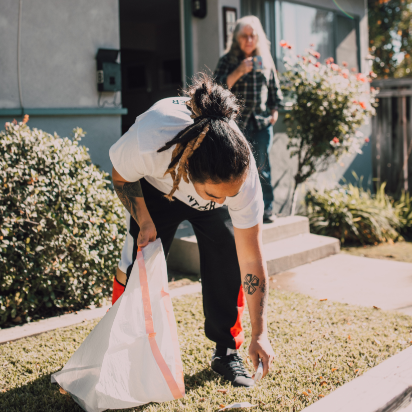 Man picking up trash while an older widowed woman looks on in gratitude