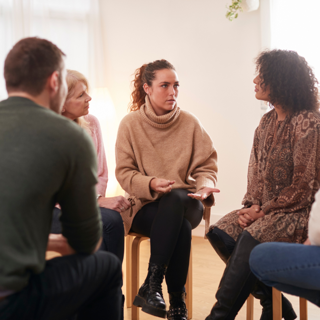 Young woman sits in group circle and leads a counseling session for widows and widowers