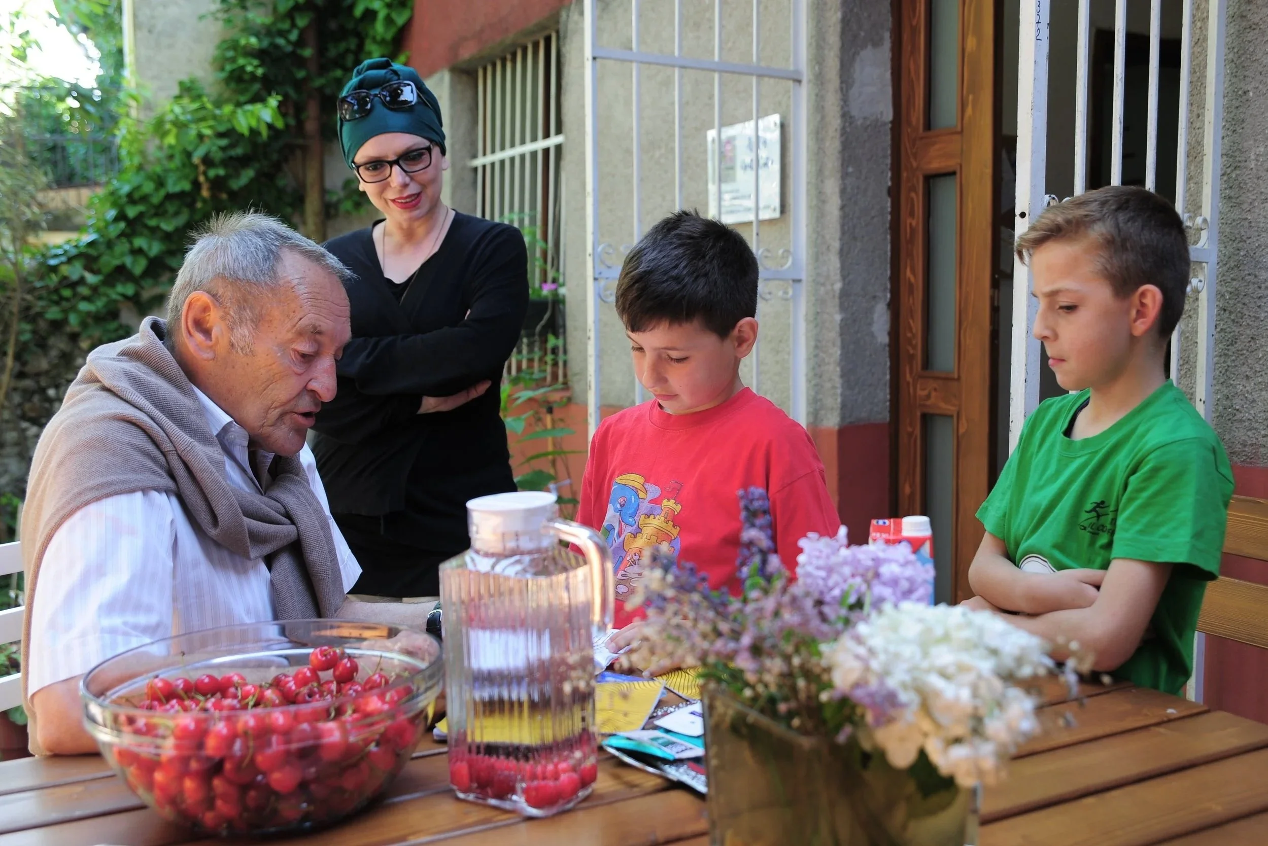 Paul Wohlgenannt sitzt draußen an einem Holztisch, umgeben von Kindern aus dem Jugendzentrum im Gespräch.