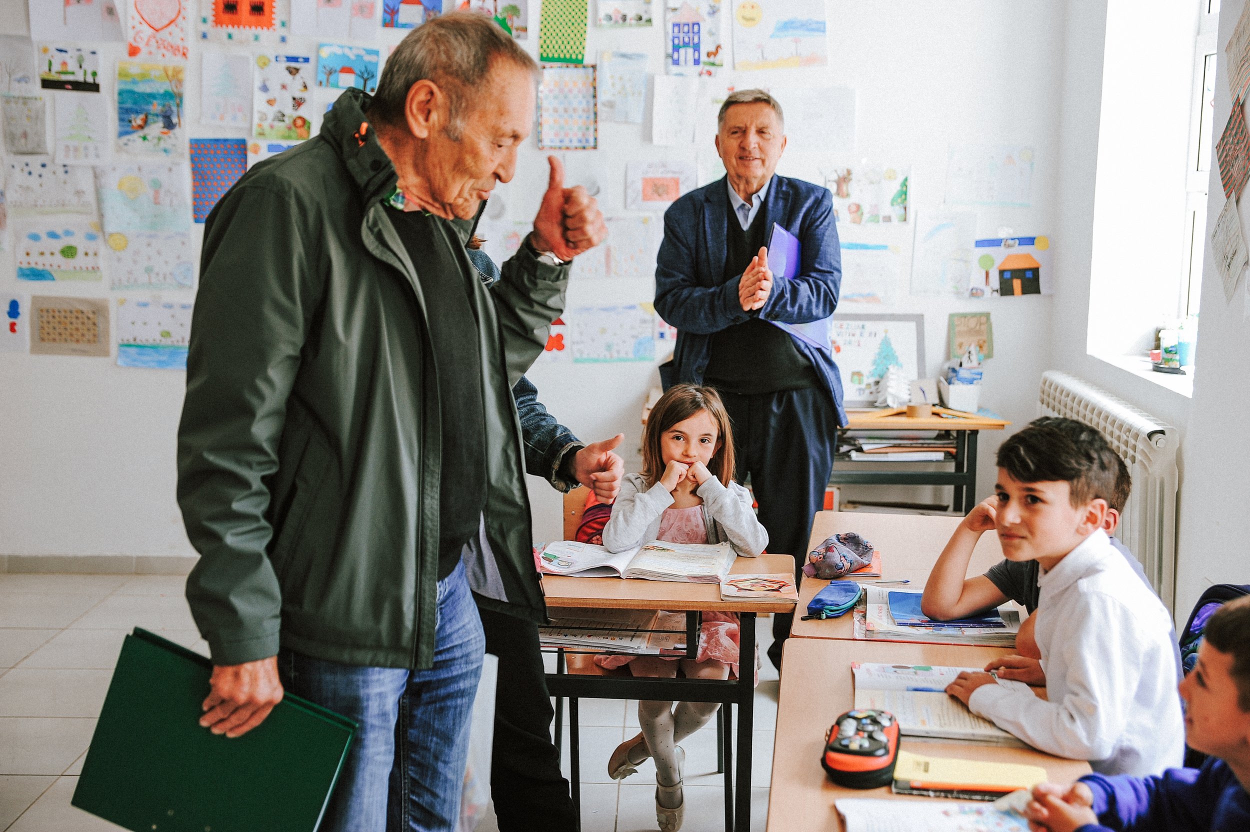 Paul Wohlgenannt spricht in einer albanischen Grundschule mit Schüler*innen, während sie im Klassenraum sitzen, der an die Wand voller Kinderzeichnungen hängt.