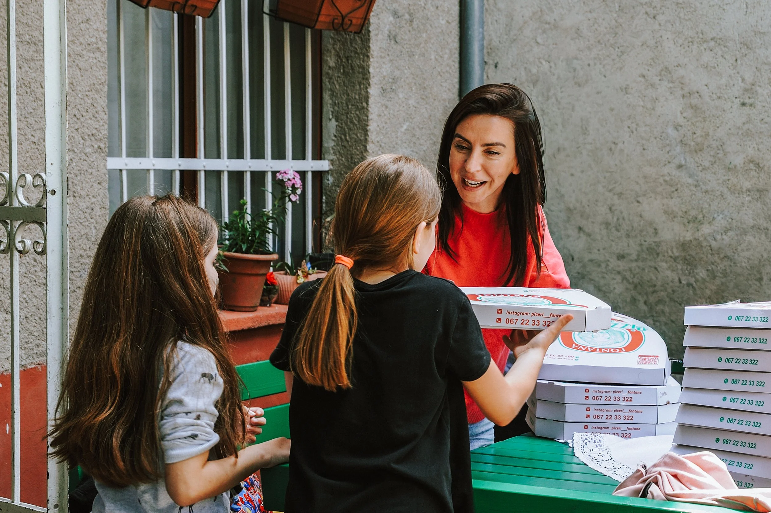 Eine Frau teilt Pizza an zwei junge Mädchen draußen an einem Tisch.