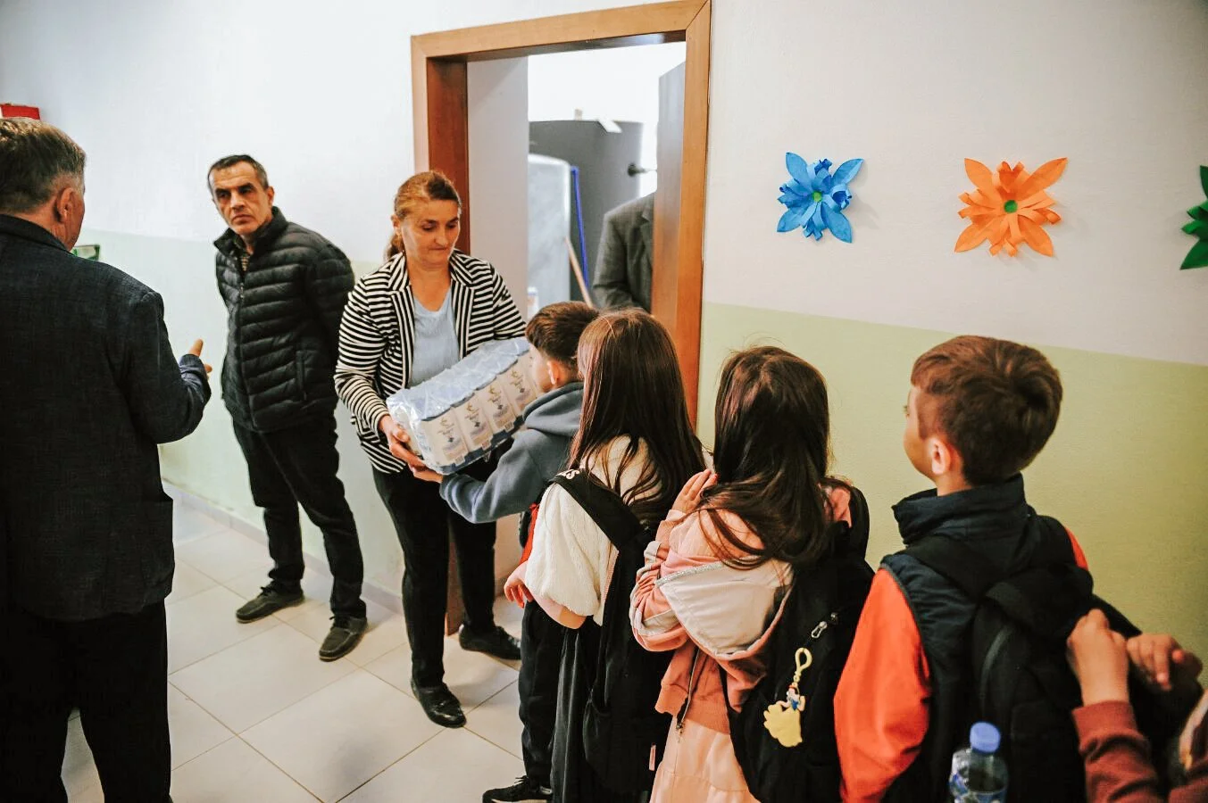 Kinder stehen in einer Reihe, um Lebensmittelhilfen zu erhalten, während Erwachsene ihnen in einem Flur einer Schule Mehl übergeben.