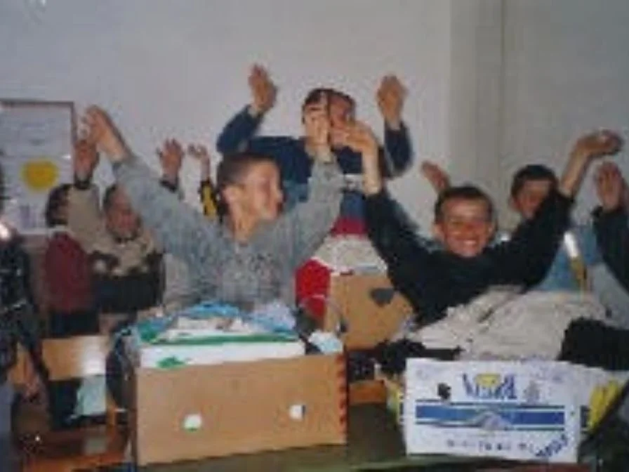 Gruppe von lachenden Menschen, die in einem Raum sitzen, einige mit erhobenen Armen in Feierlaune.