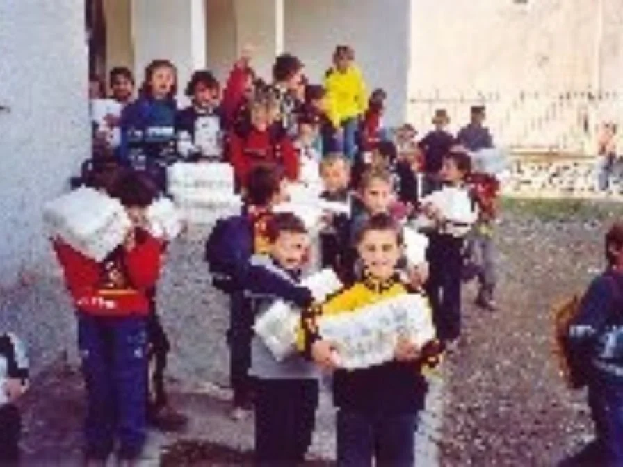 Kinder, die Geschenke, vermutlich zu Weihnachten, vor einem Gebäude tragen.