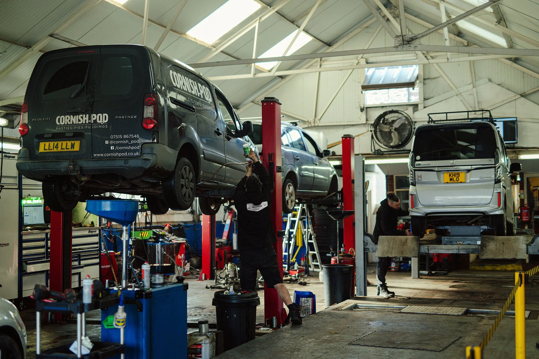Auto repair shop with cars on lifts and mechanics working underneath and around them in a spacious indoor garage.