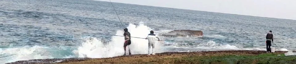 Pessoas pescando na orla de uma praia com ondas quebrando na costa.
