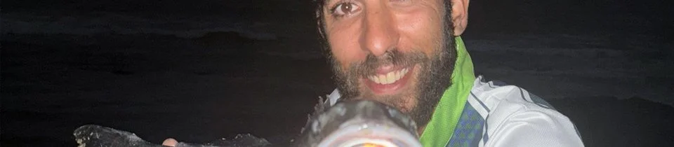 Homem com barba sorrindo segurando um peixe à noite