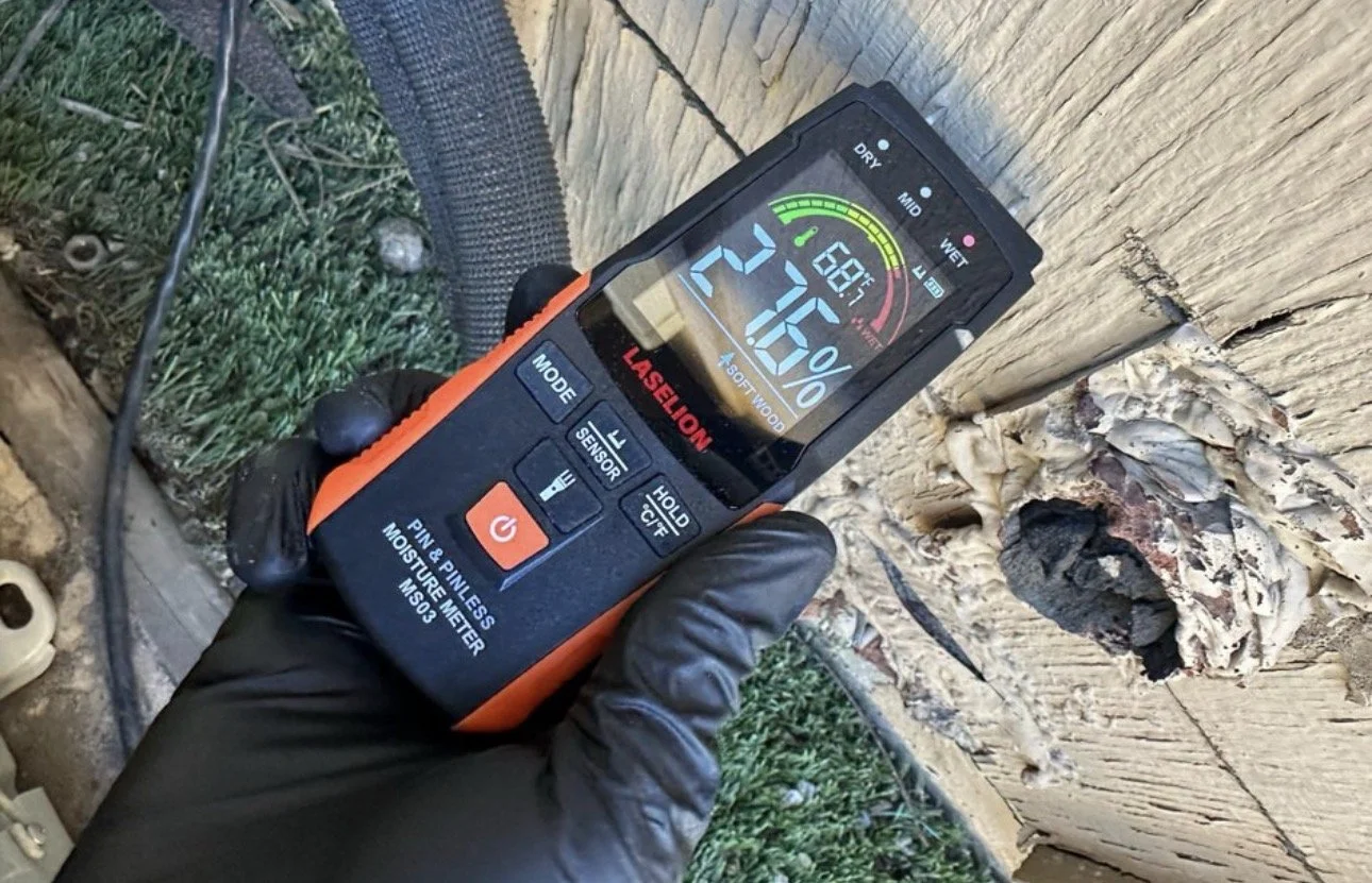 A person holding a laserhybrid moisture meter measuring moisture content in a wooden beam outdoors.