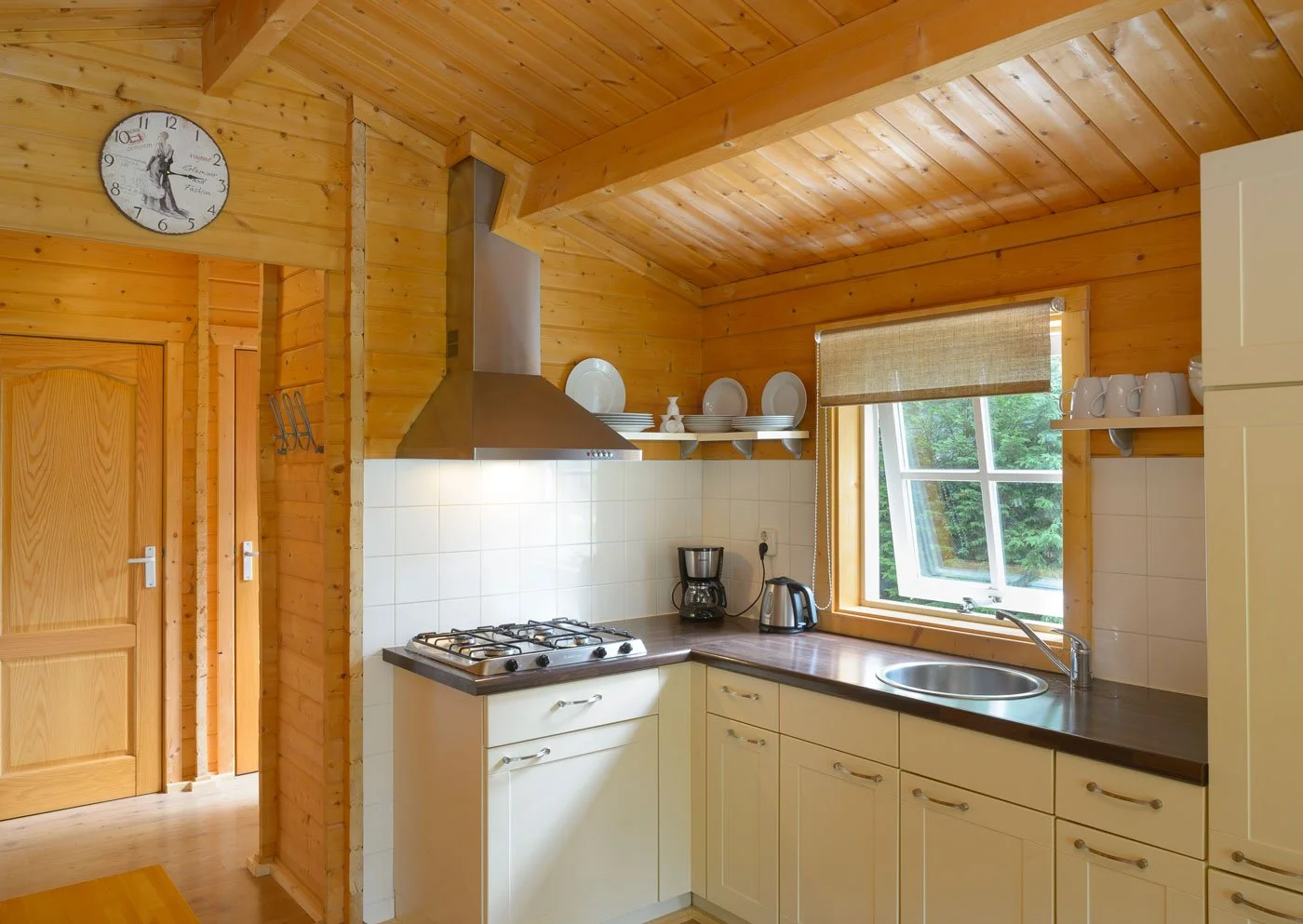 Wood-paneled kitchen with white cabinets, a countertop with kitchen appliances, open window, and wall clock.